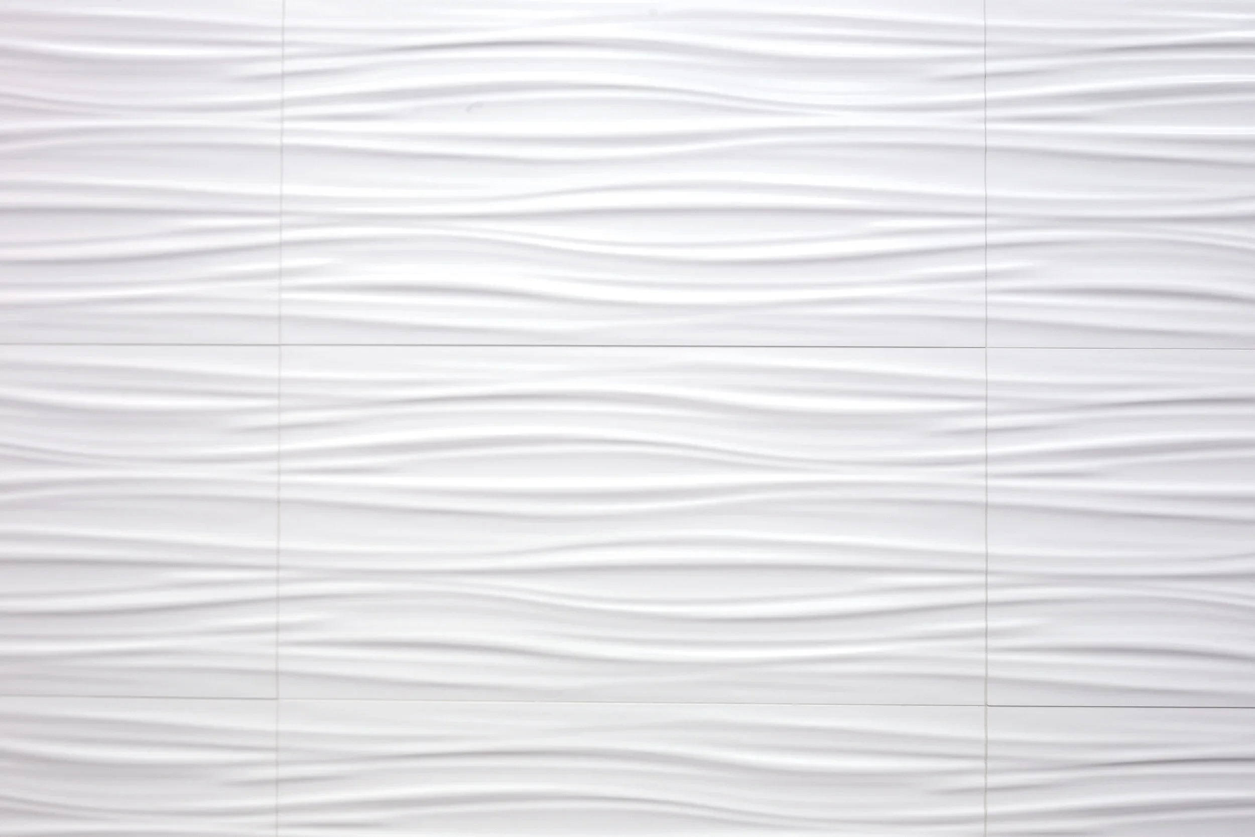 Close-up of a wall with 3D textured white tiles featuring wavy horizontal lines
