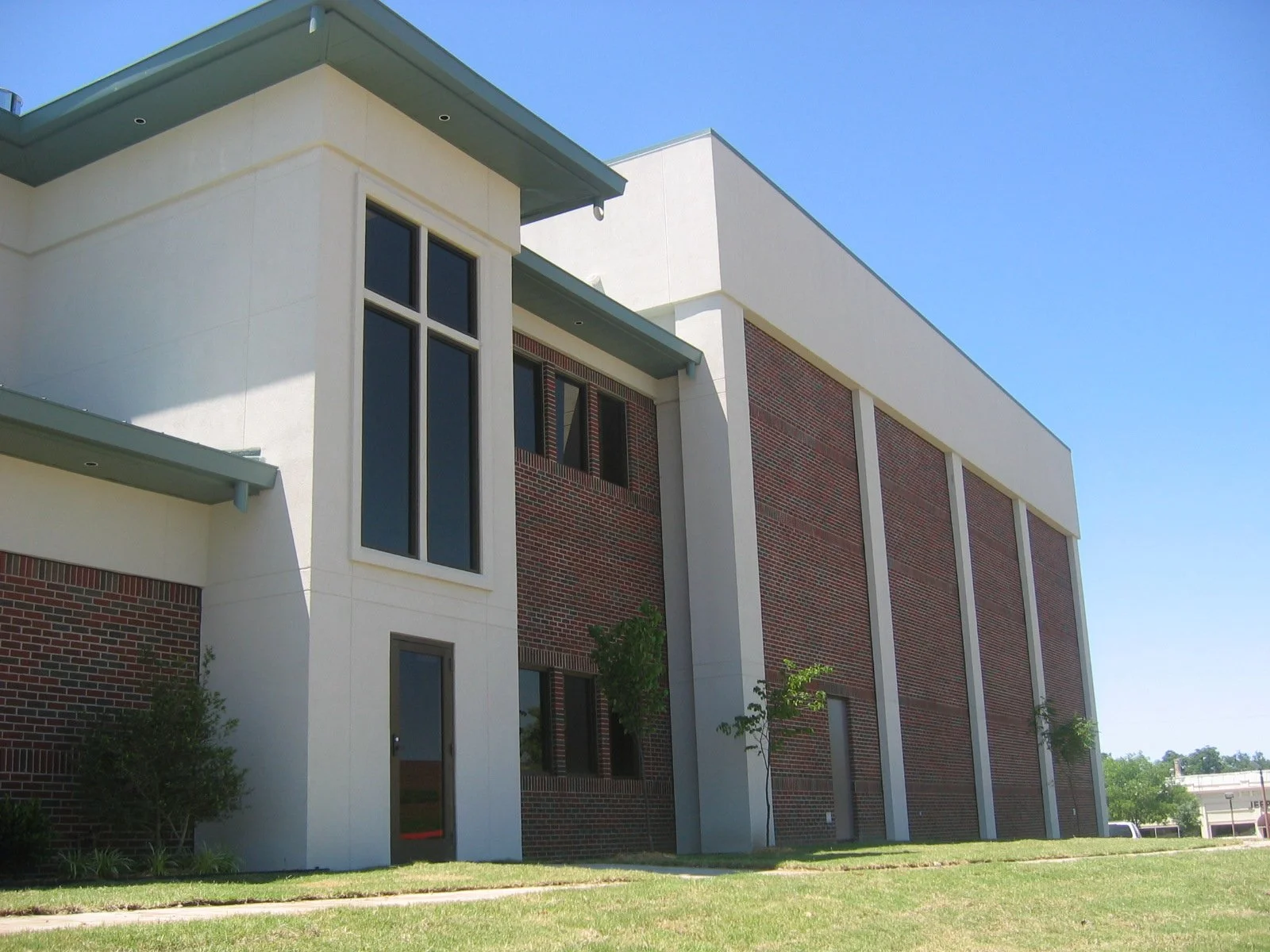 Modern building with a brick and white exterior, large windows, and a small lawn in front under a clear blue sky.