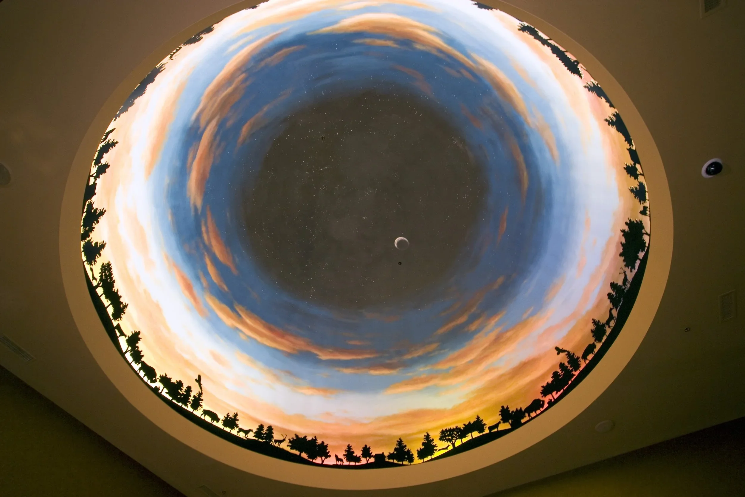 Ceiling with a mural of a sunset sky and a forest silhouette, with a starry night sky and planets in the center.
