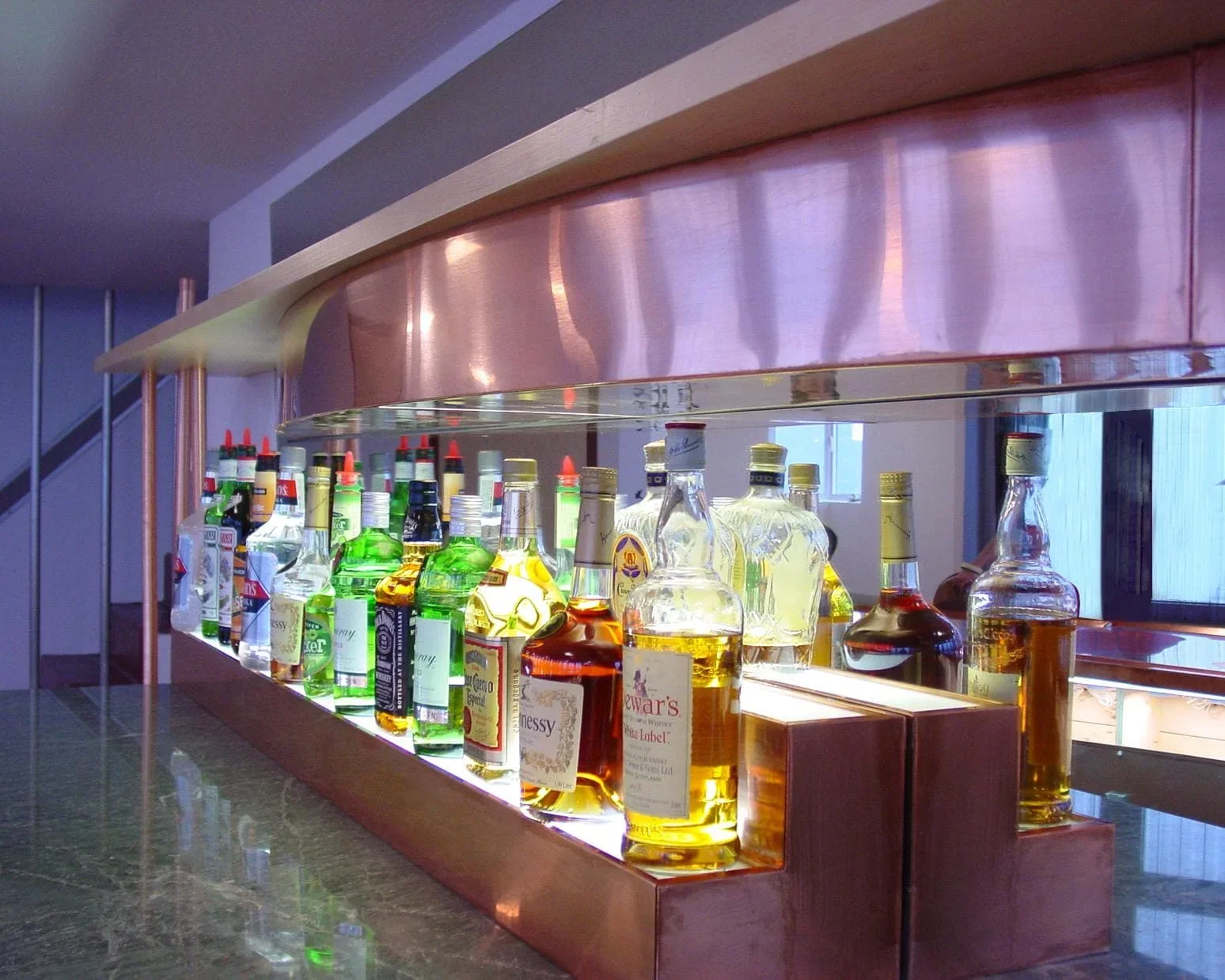 Assorted bottles of liquor on a backlit wooden bar shelf.