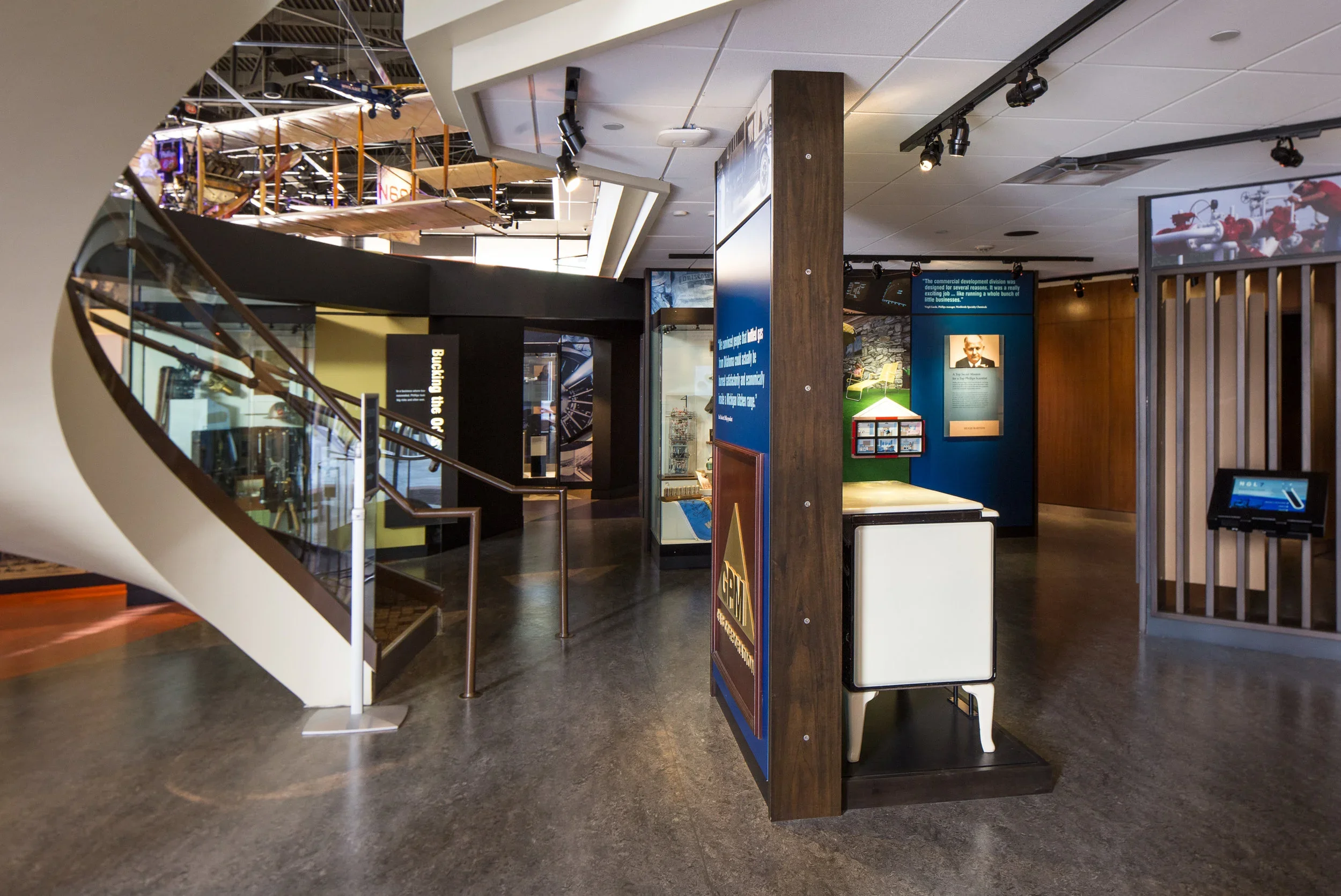Interior of a museum exhibit space featuring informational displays, a staircase with glass railing, and various display cases and panels.