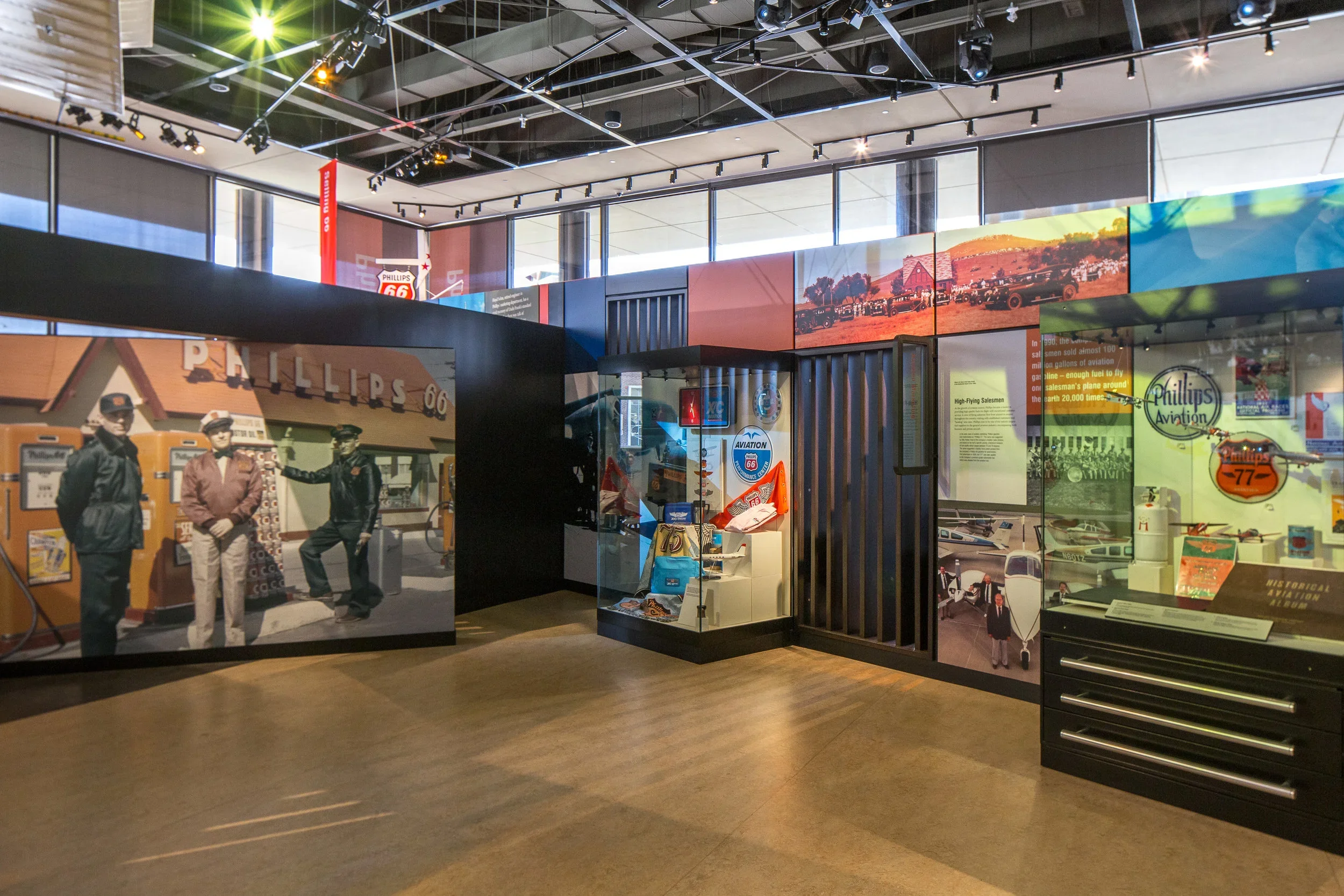 Interior of a museum exhibit featuring historical photographs, memorabilia, and displays related to aviation and Route 66, with large windows letting in natural light.