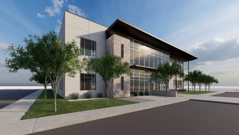 Modern two-story commercial building with large glass windows, surrounded by small trees and greenery, under a partly cloudy sky.