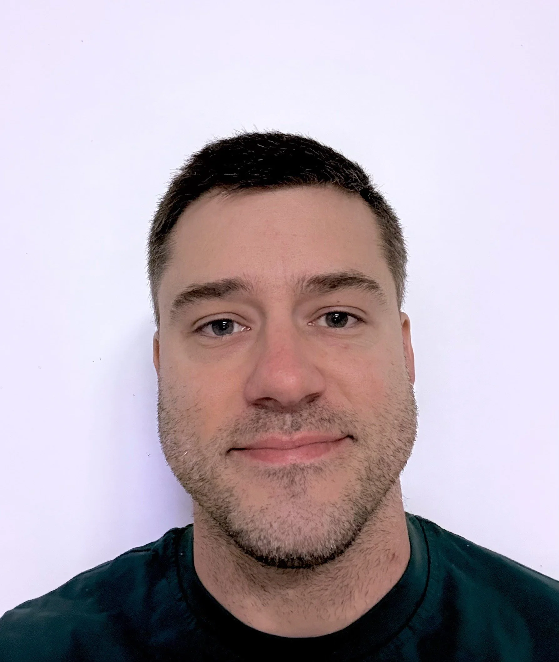 A man with short dark hair and a light beard looking at the camera against a plain white background.