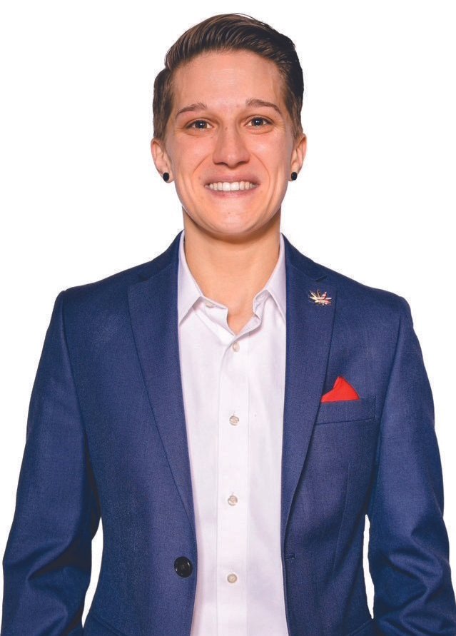 A young man with short slicked-back hair, wearing a navy blue blazer with a lapel pin, a white collared shirt, and a red pocket square, smiling confidently against a white background.
