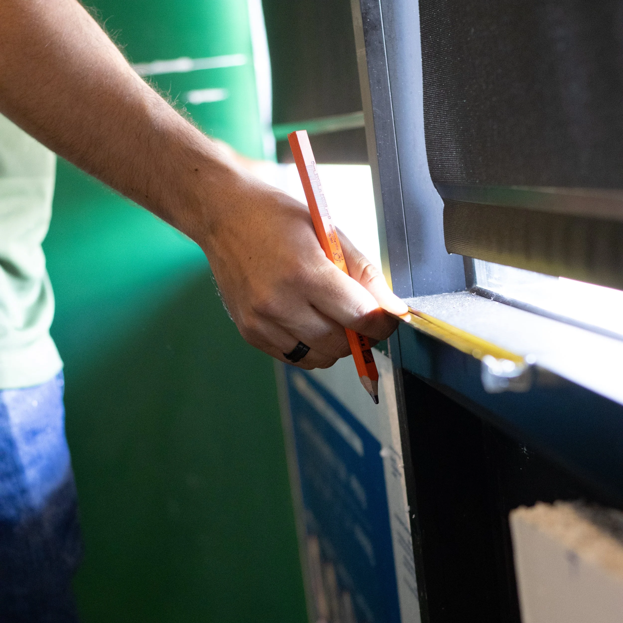 A person measuring a surface with a yellow ruler near a window.