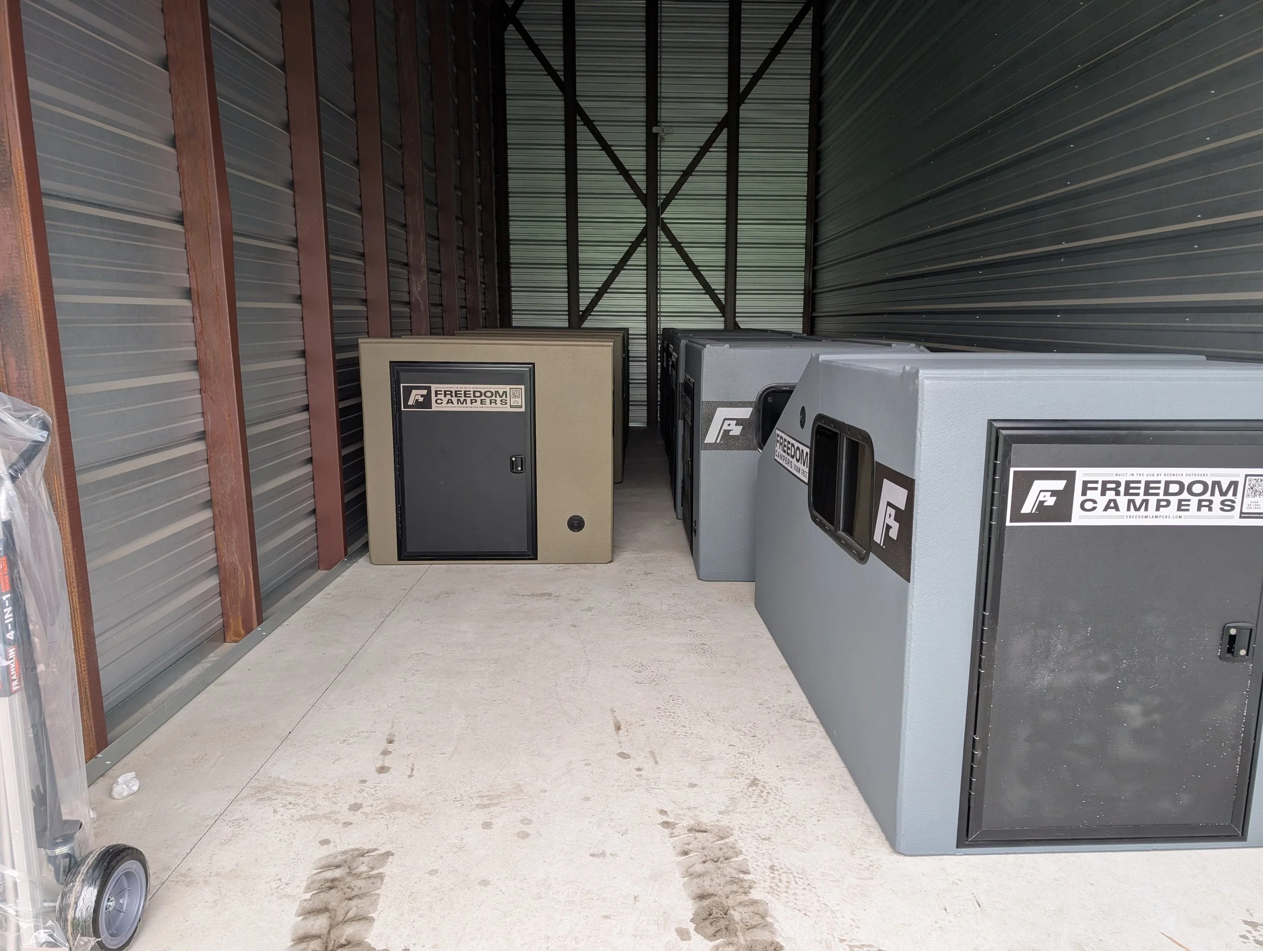 Indoor storage unit containing multiple portable camping coolers with 'Freedom Campers' labels.