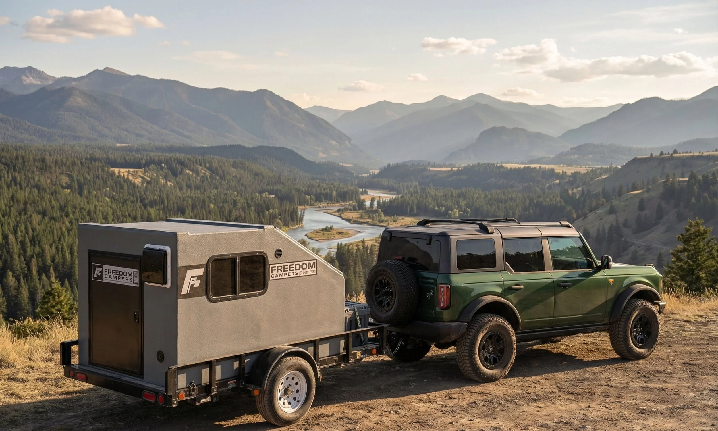 A green off-road vehicle towing a camper trailer on a dirt path in a mountainous landscape with a river flowing through the valley below.