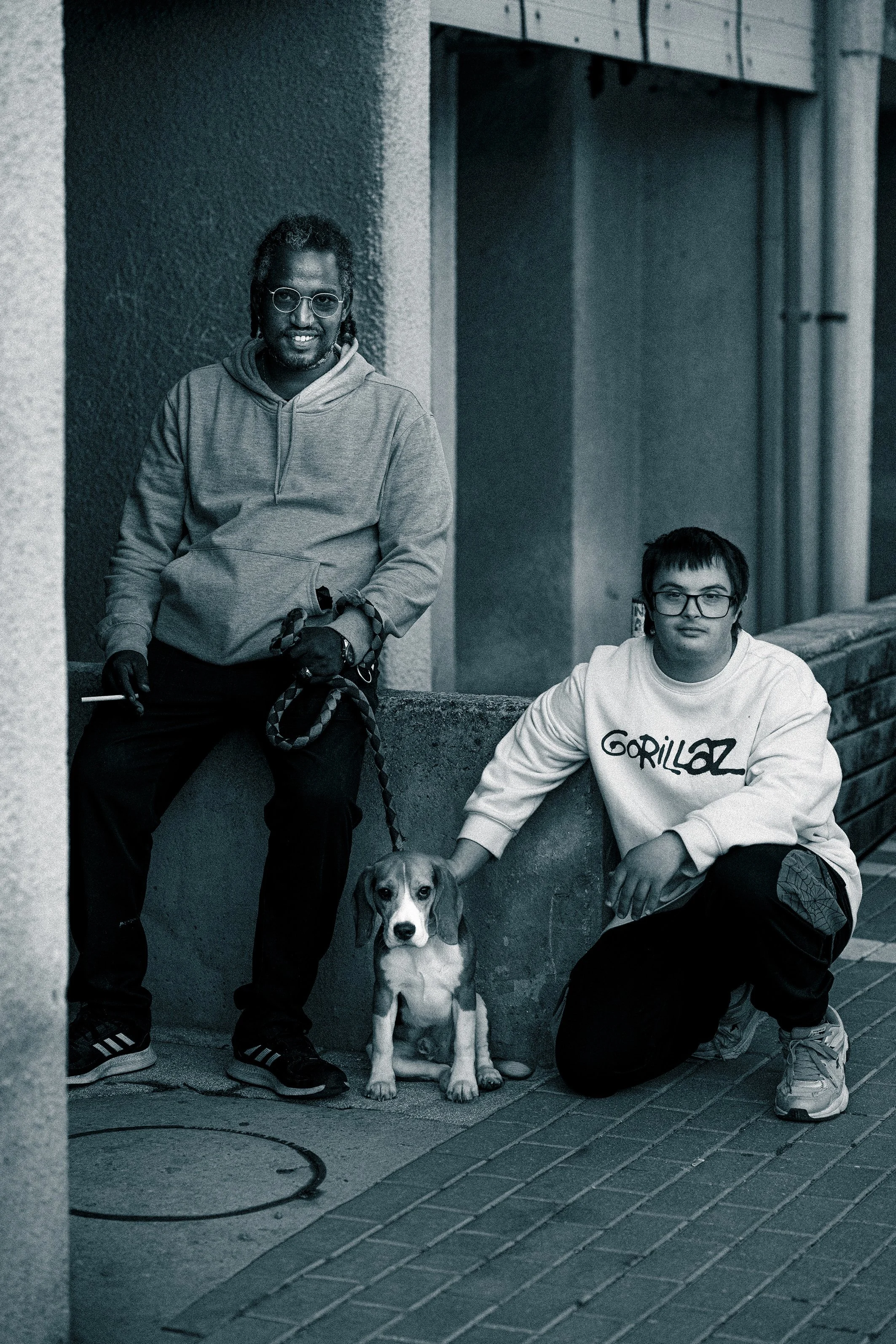 black man sitting near building with the dog and Down syndrome kid sitting next to dog and petting it