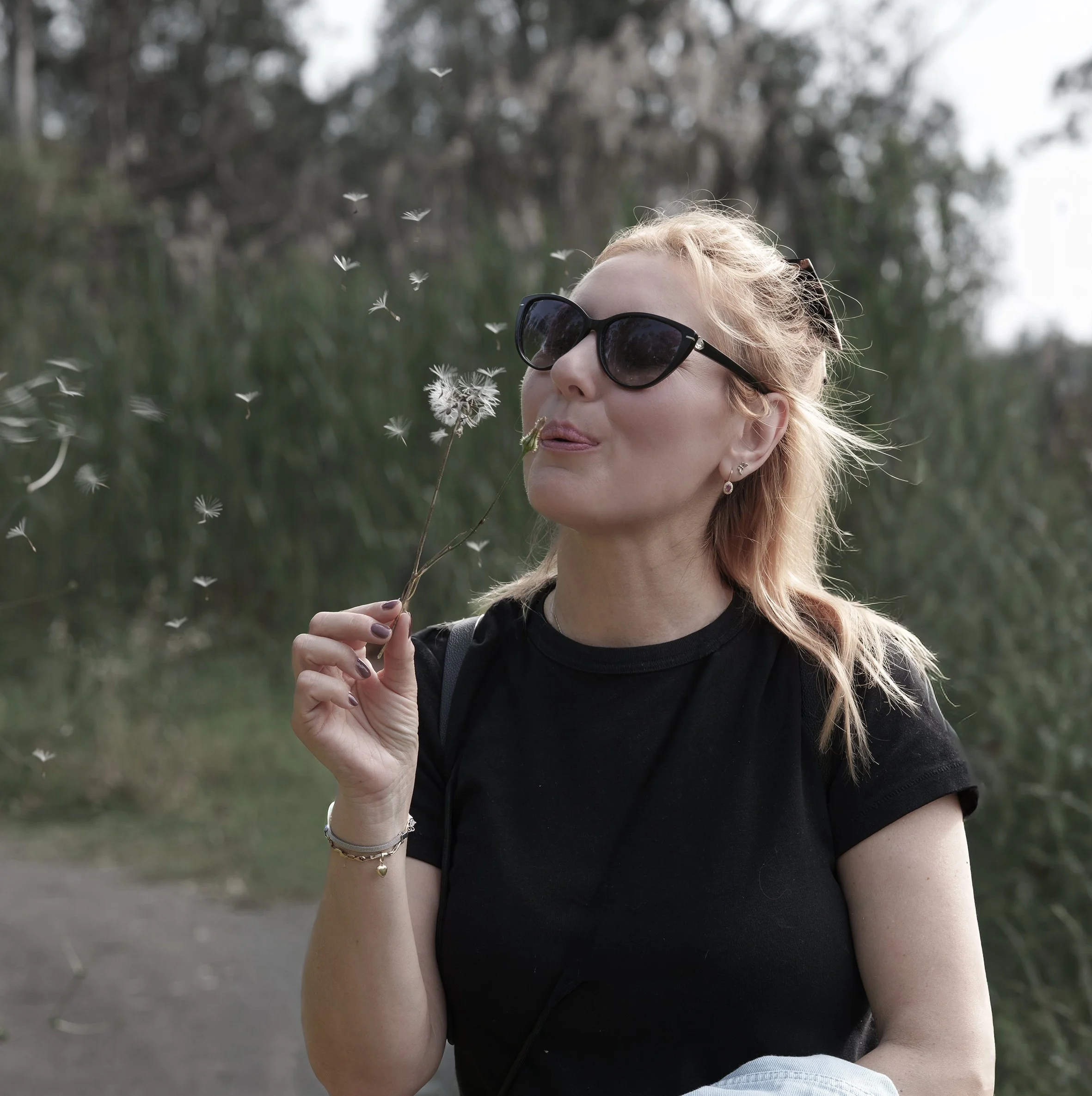 a young woman on nature background blowing dandelion and smiling 