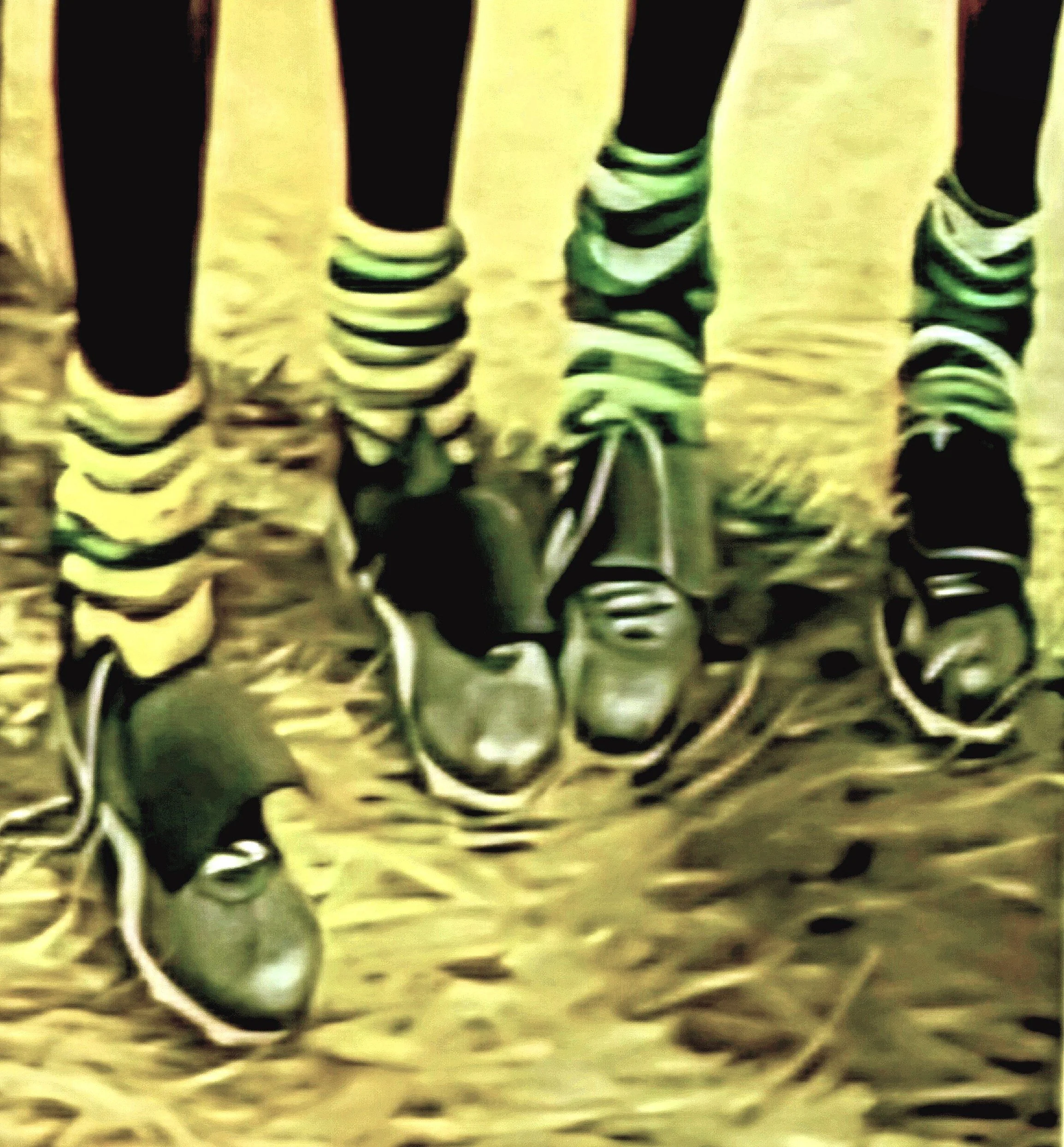 Close-up of the legs and feet of four people wearing sneakers and socks, standing on a dirt or sandy ground.