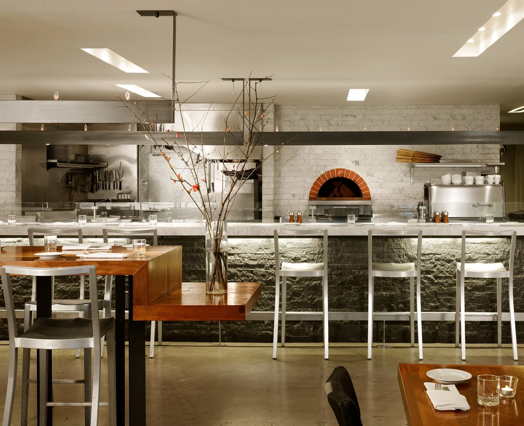 Local Wine Merchant restaurant and bar in San Francisco. Everything custom fabricated. Stainless steel kitchen area with a brick oven and utensils, along with marble walls and ceiling lights.