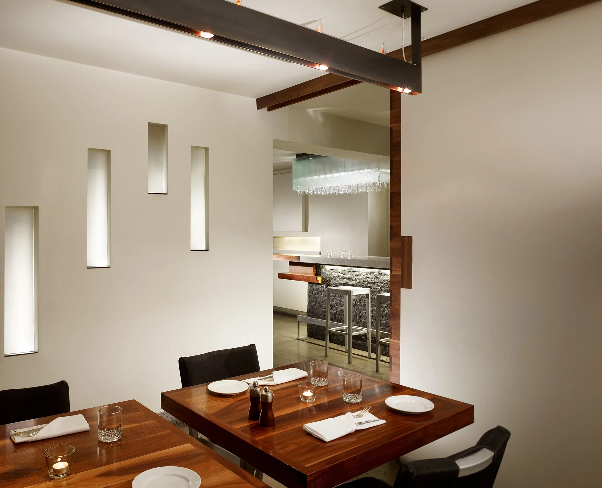 Local Wine Merchant restaurant and bar in San Francisco. Custom fabricated modern dining area with a wooden table set for a meal, featuring plates, glasses, and napkins.