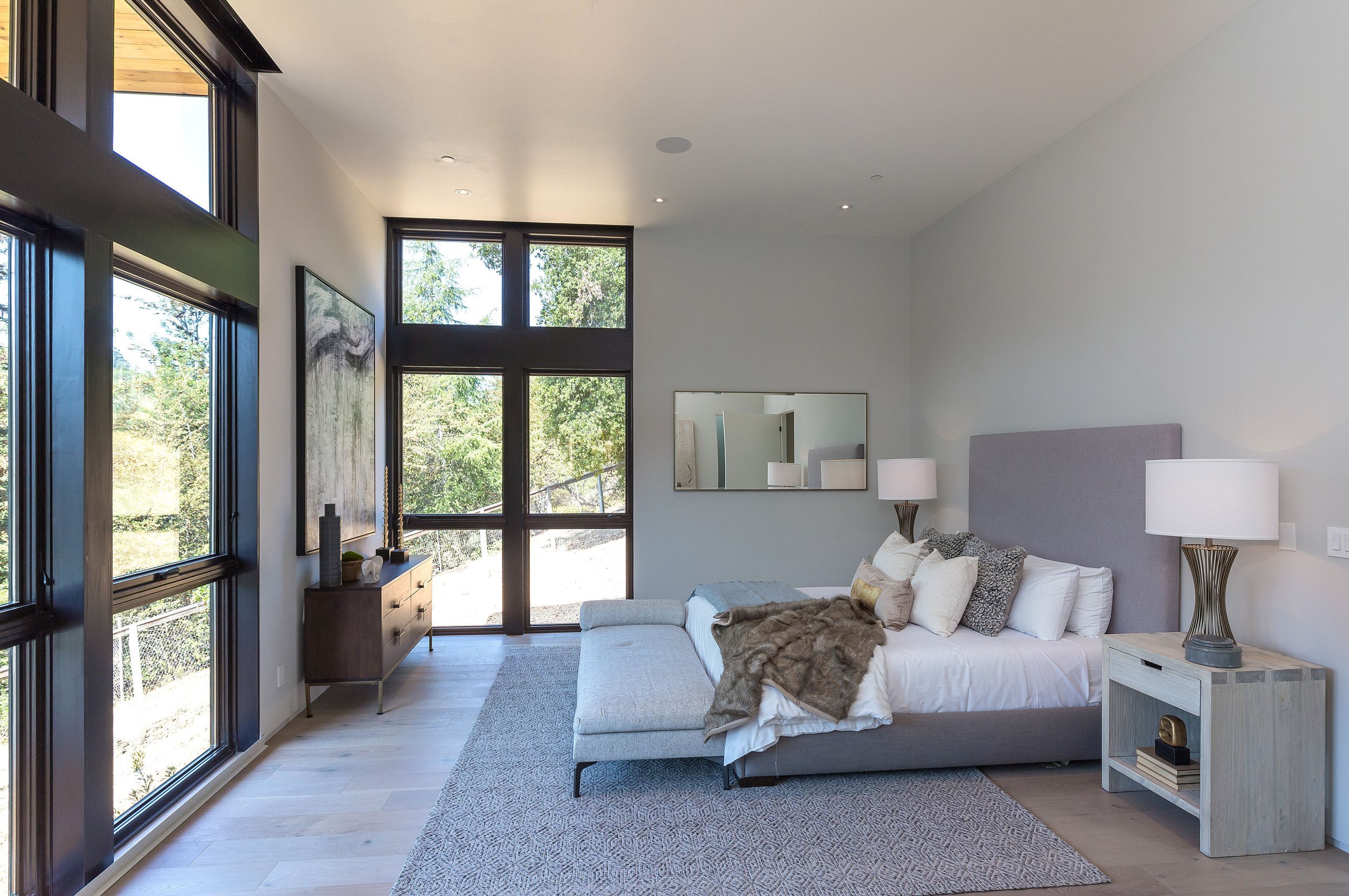 Los Altos Hillside Home in Los Altos, California. Modern bedroom with large windows, white walls, wooden furniture, and neutral-toned bedding.