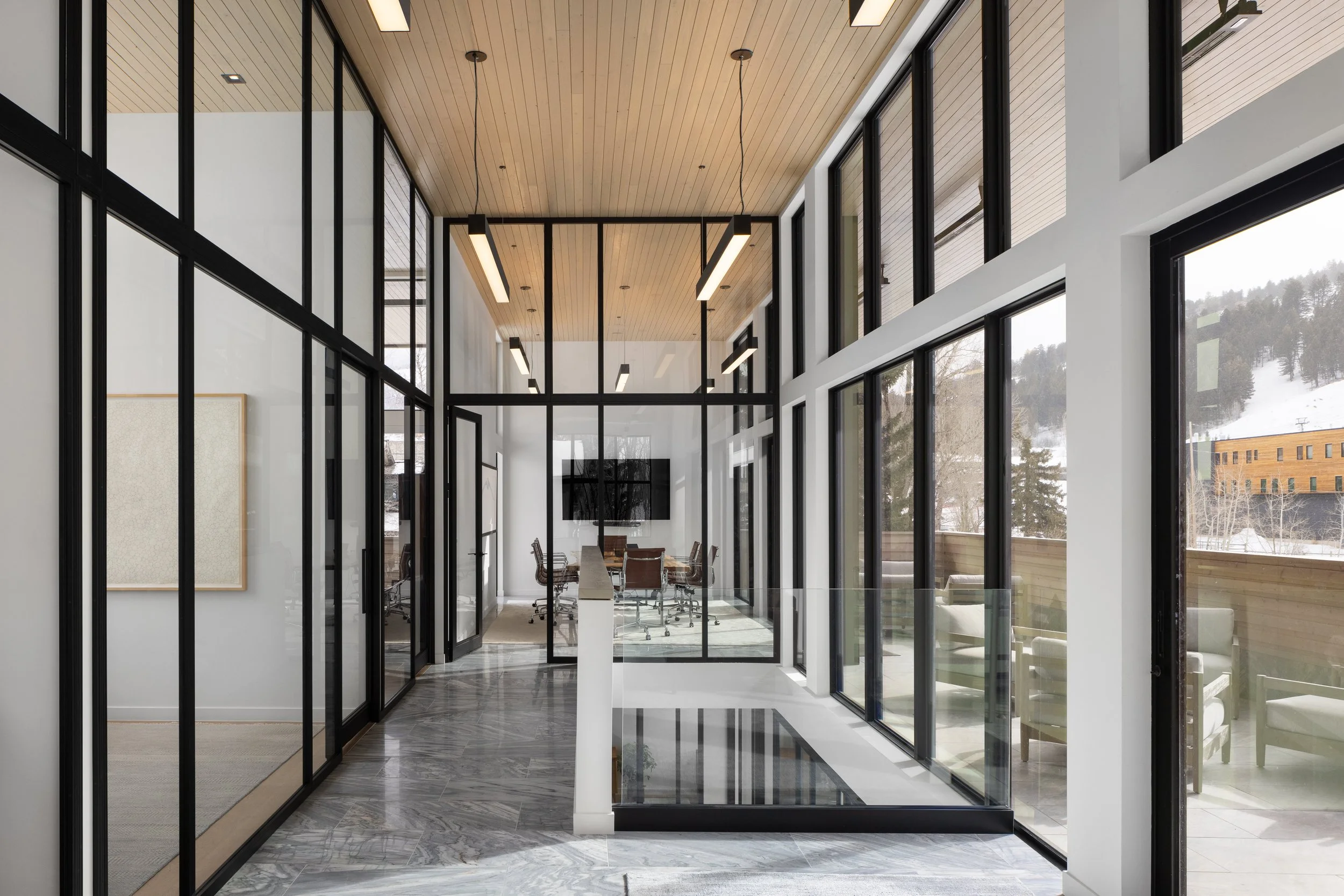 Office at Snow King in Jackson, Wyoming. Modern office interior with large glass walls and a conference room with a long table and chairs, overlooking snowy landscape outside.