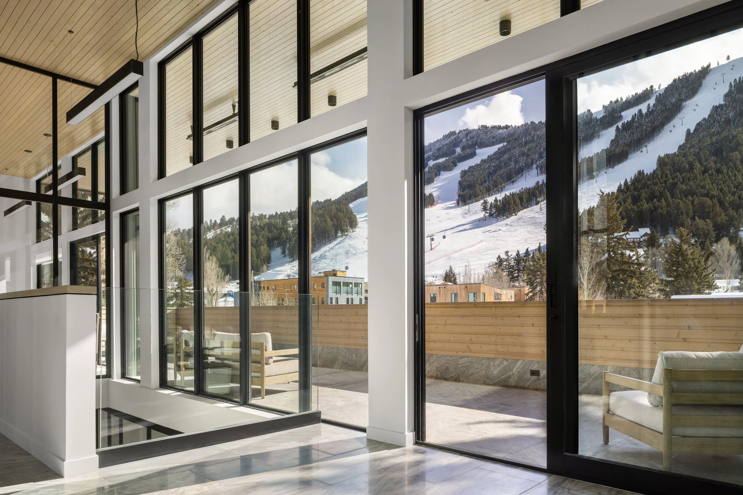 Office at Snow King in Jackson, Wyoming. Modern interior living space with large floor-to-ceiling windows overlooking a snowy mountain landscape with trees and ski slopes.