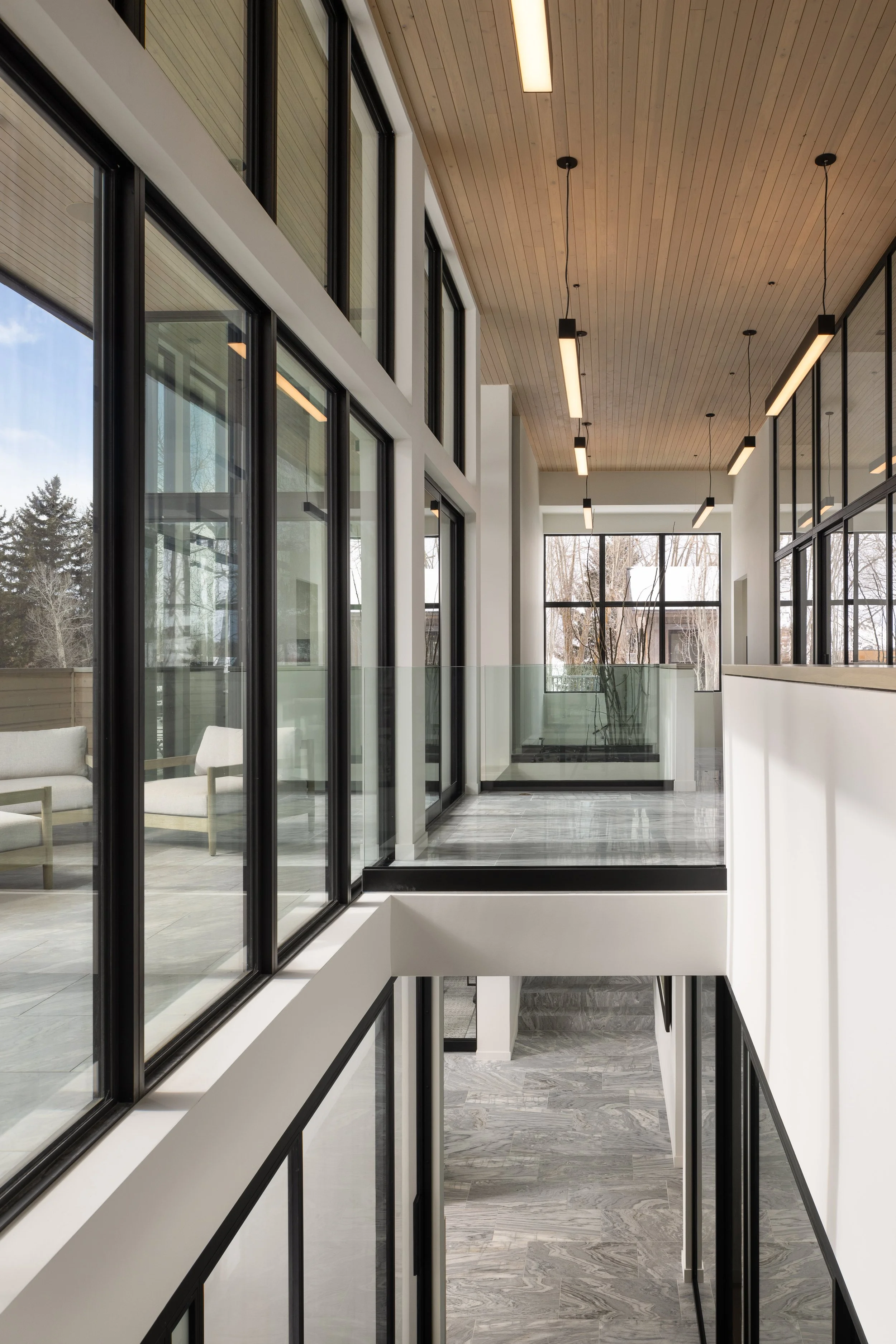 Office at Snow King in Jackson, Wyoming. Interior view of a modern building with large glass windows, a wooden ceiling with linear lighting, and a corridor with marble flooring.