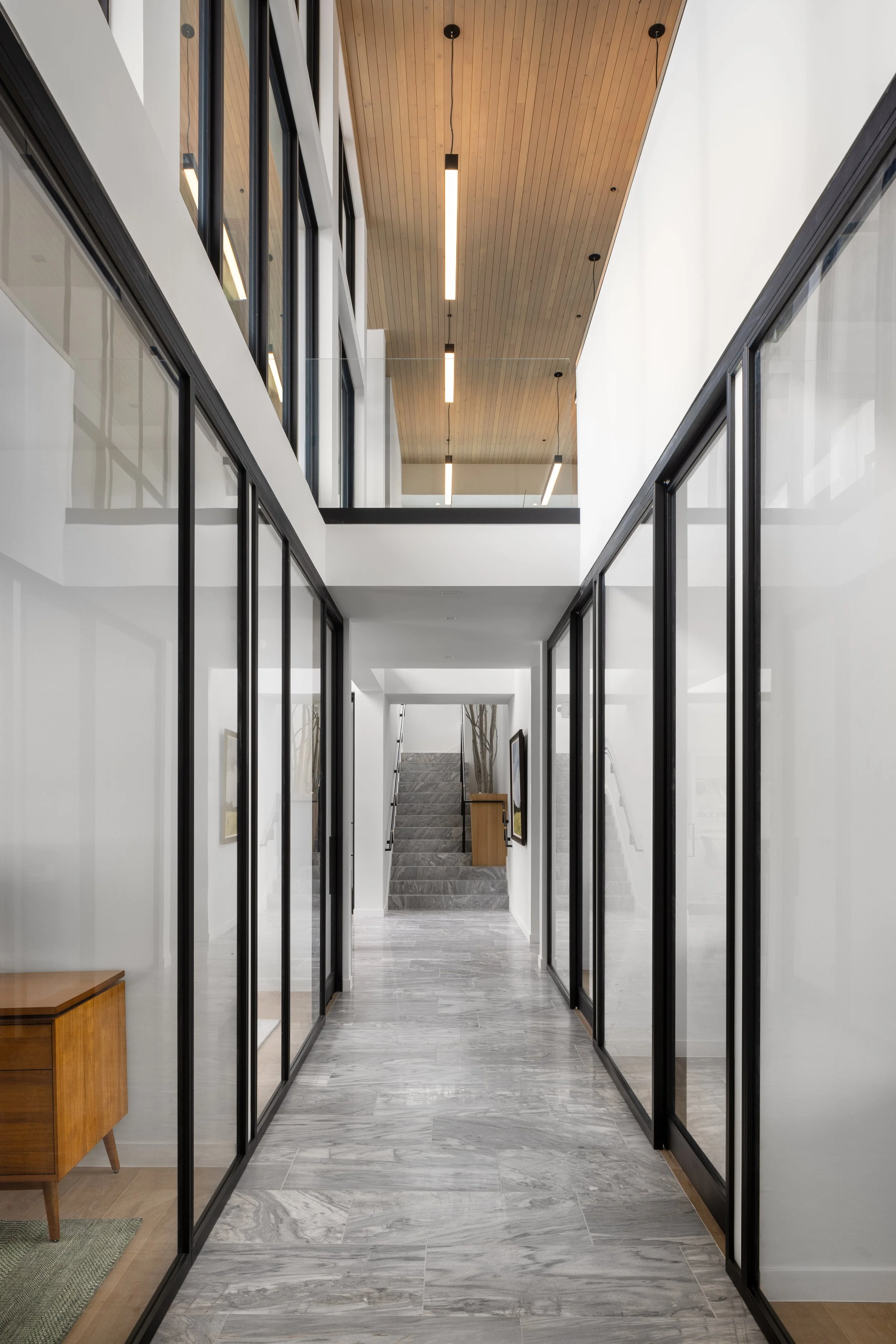 Office at Snow King in Jackson, Wyoming. Modern indoor hallway with glass-walled office partitions, a staircase at the end, and a wooden ceiling with hanging lights.
