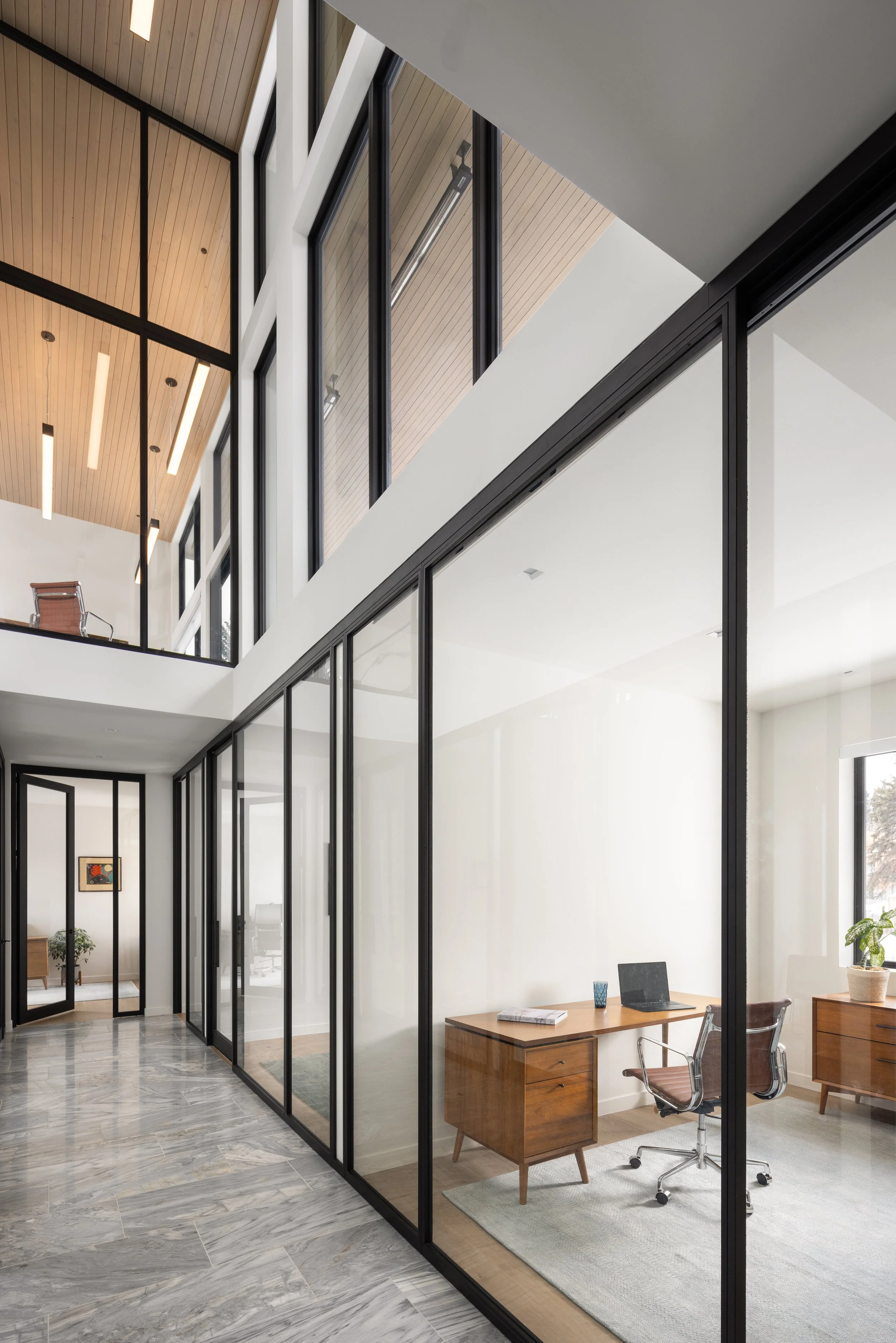 Office at Snow King in Jackson, Wyoming. Modern office with glass walls, a wooden ceiling, and marble flooring, featuring a workspace with desk, chair, and plants.
