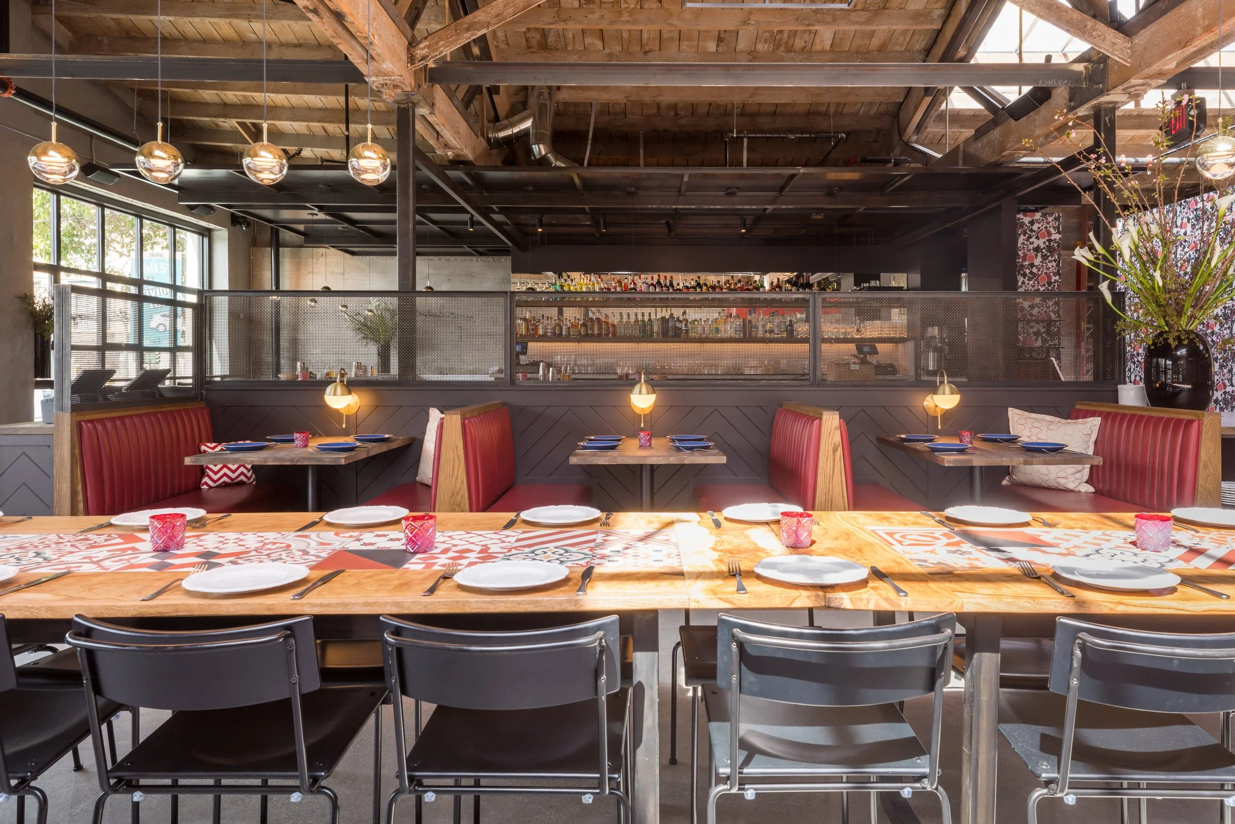 Che Fico restaurant in San Francisco, California. A restaurant interior with a large wooden table set with plates, forks, and pink candle holders.