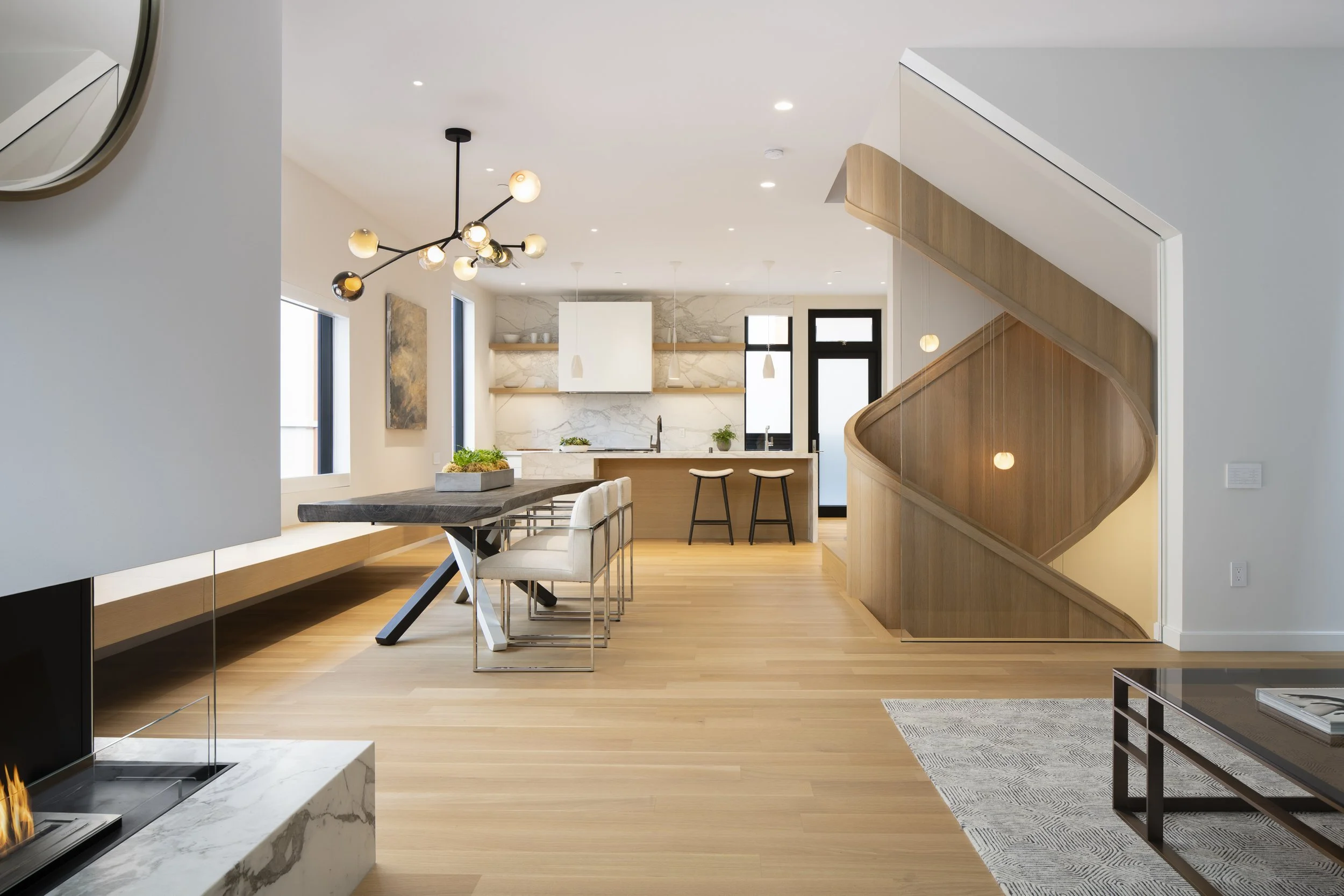 Six-Story City House in San Francisco, California. Modern open-concept living and dining area with wooden floors, white walls, a staircase with wooden railing, and stylish lighting fixtures.