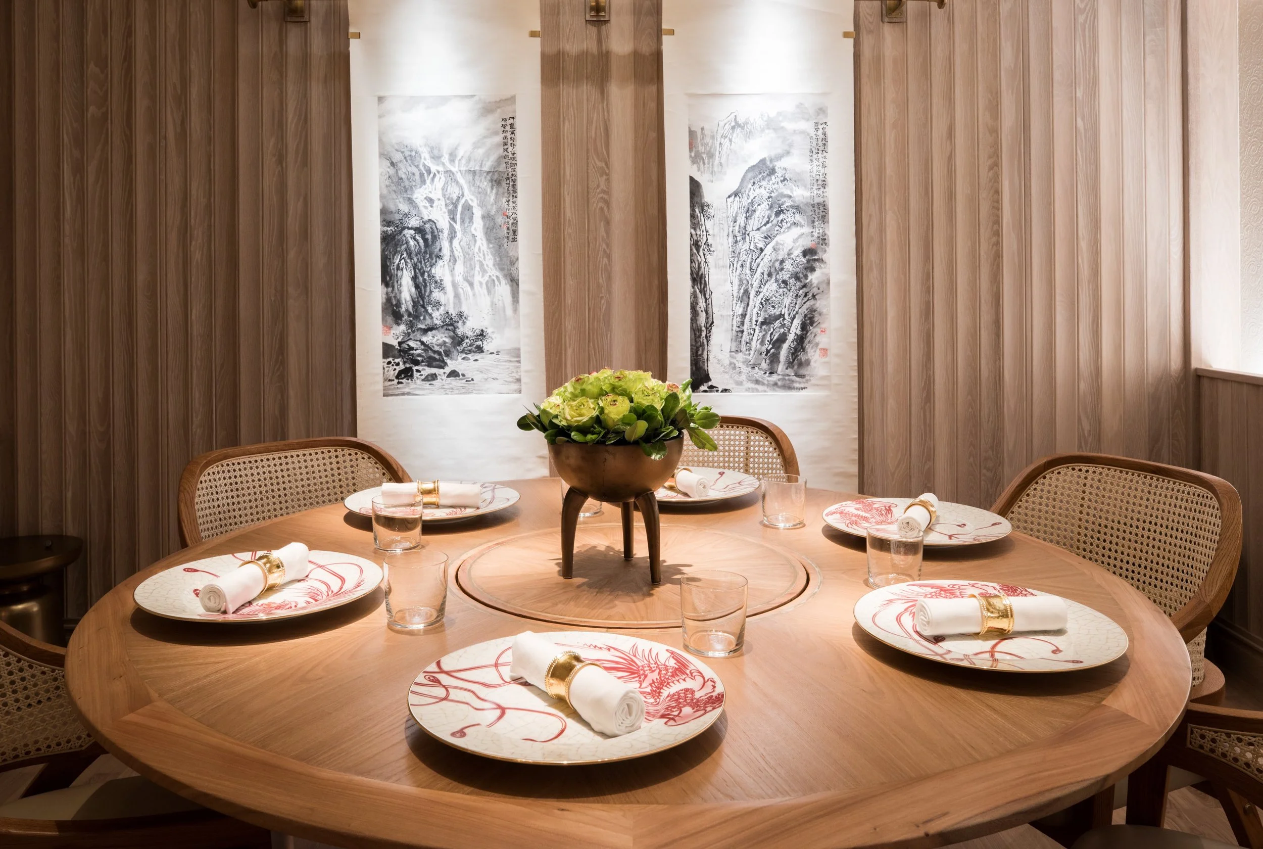 Eight Tables restaurant above China Live Market in San Francisco, California. A round wooden dining table set for a meal with plates, glasses, and napkins.