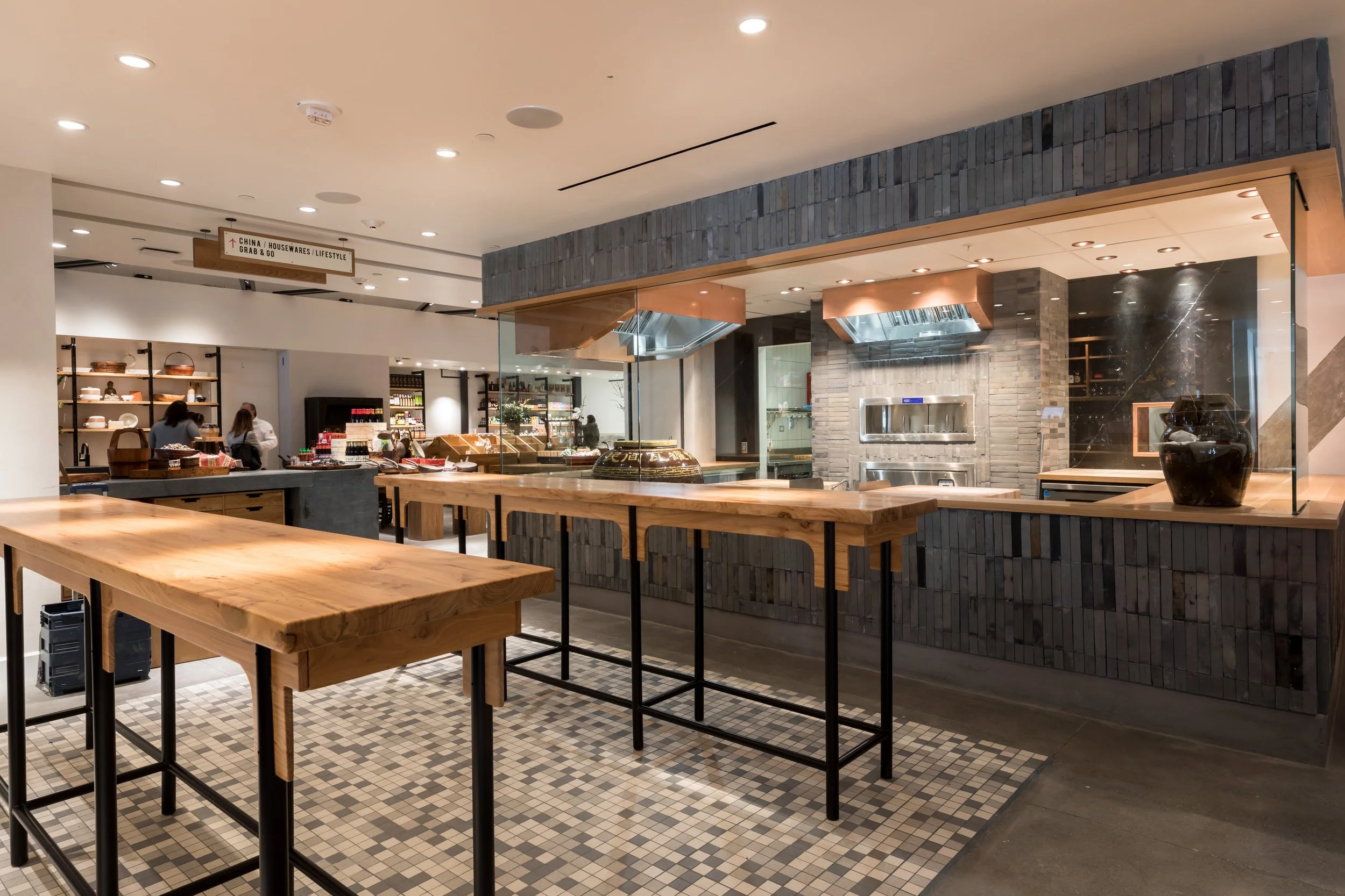 China Live Market in San Francisco, California. Experiential retail. Interior of a modern restaurant or cafe with wooden tables, some high-top, and a tiled floor.