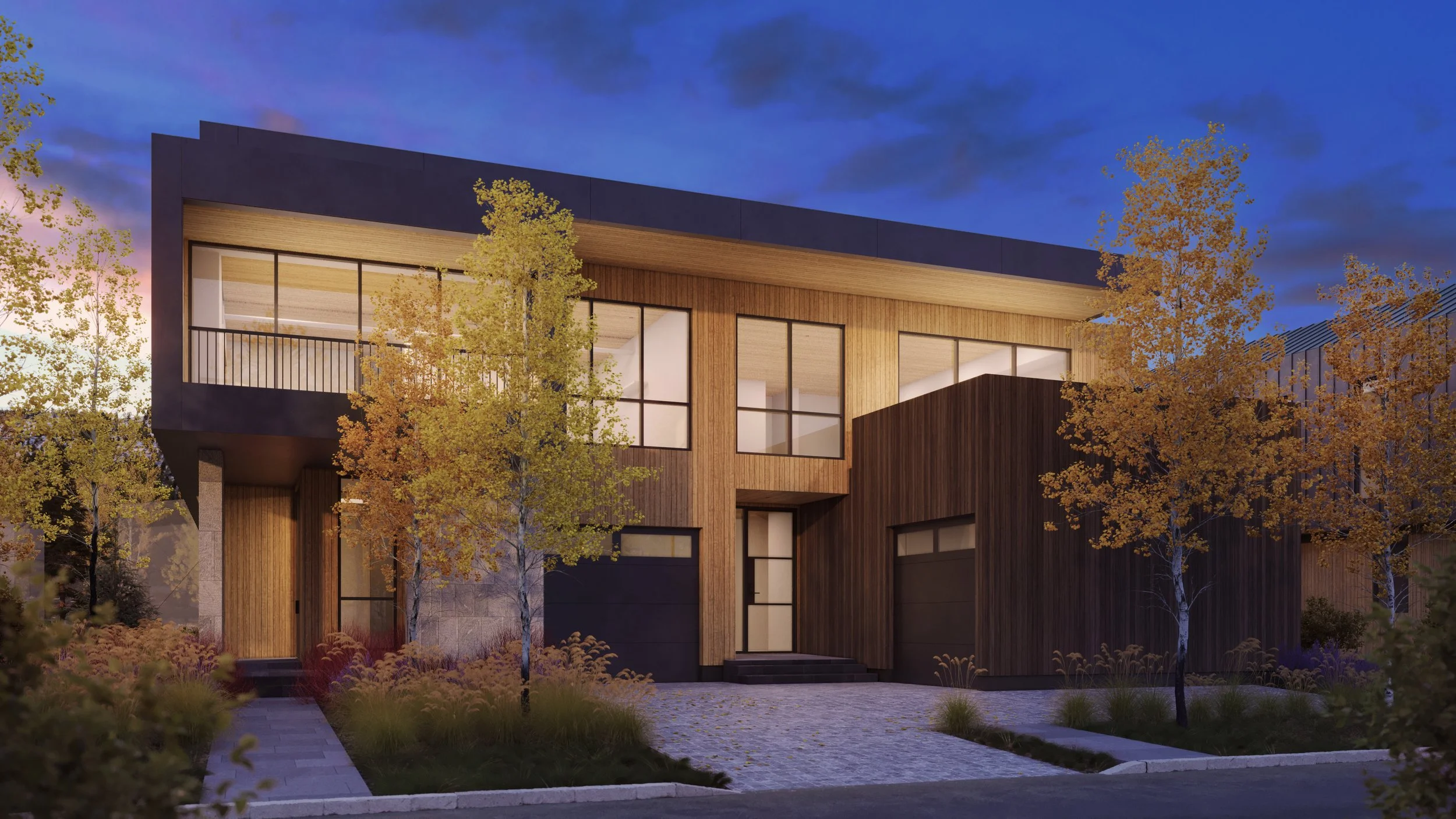 Jackson Development in Jackson, Wyoming. Modern house with large windows and wooden exterior, surrounded by trees with autumn foliage, at dusk.