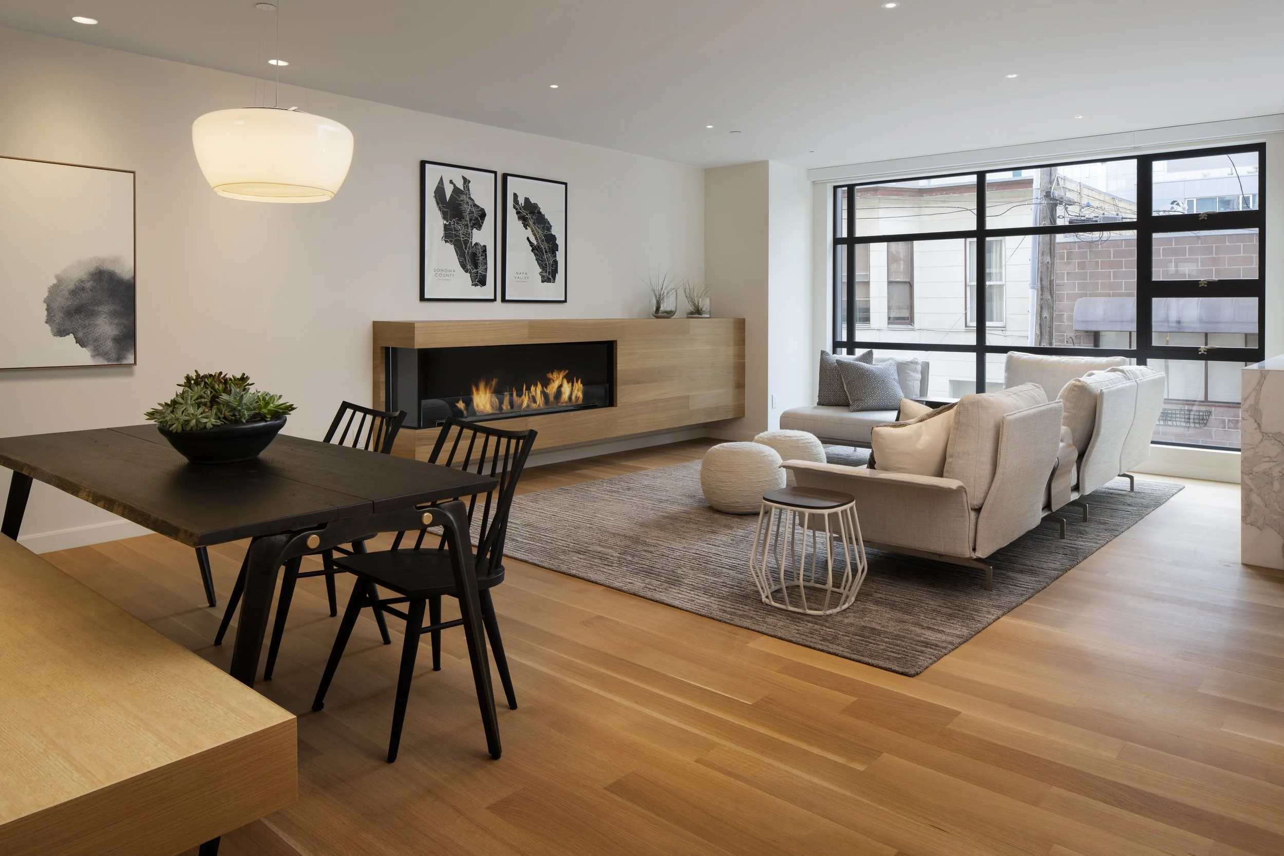 Six-Story-City House in San Francisco, California. Modern living room with large windows, beige sofa, black coffee table, fireplace, and artwork on the wall.