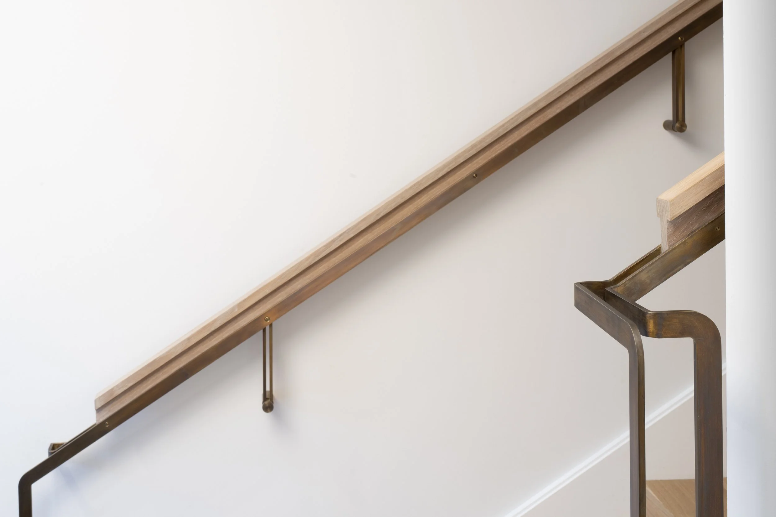 Six-Story-City House in San Francisco, California. Wooden stair handrail with metal supports along a white wall.
