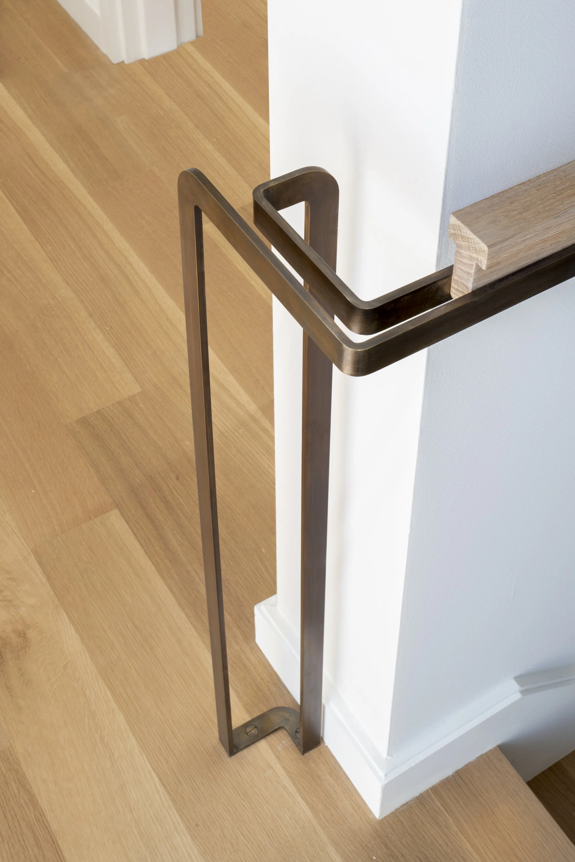 Six-Story-City House in San Francisco, California. Close-up of a stair banister with a wooden handrail and black metal balusters in a modern interior, near a corner with hardwood flooring and white walls.