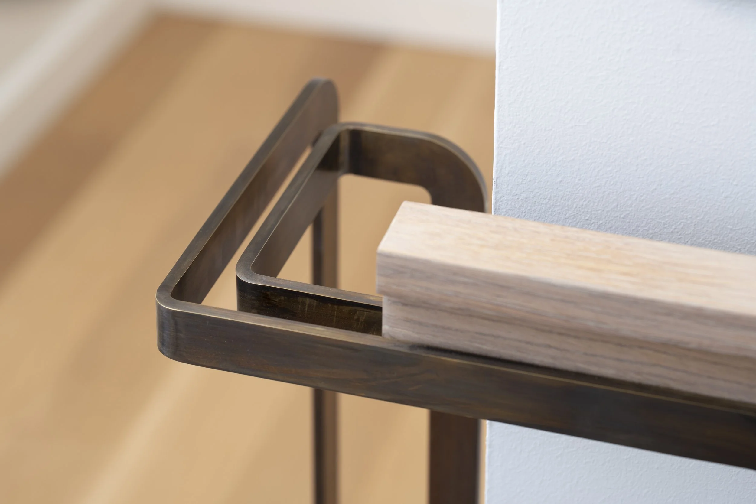 Six-Story-City House in San Francisco, California. Close-up of a black metal frame beside a light-colored wooden tabletop, against a textured off-white wall.