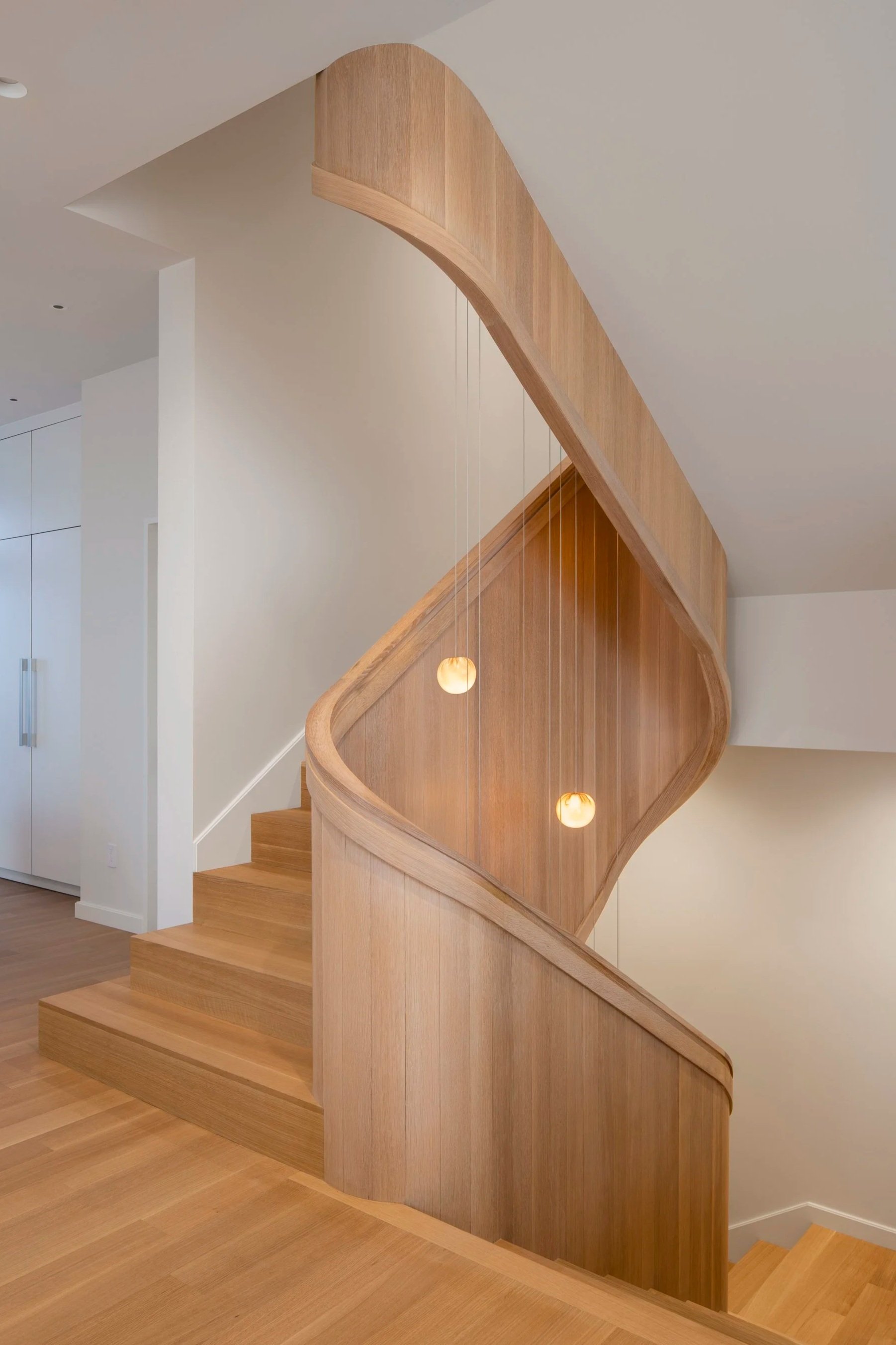Six-Story City House in San Francisco, California. Interior view of a wooden staircase with curved railing and hanging pendant lights.