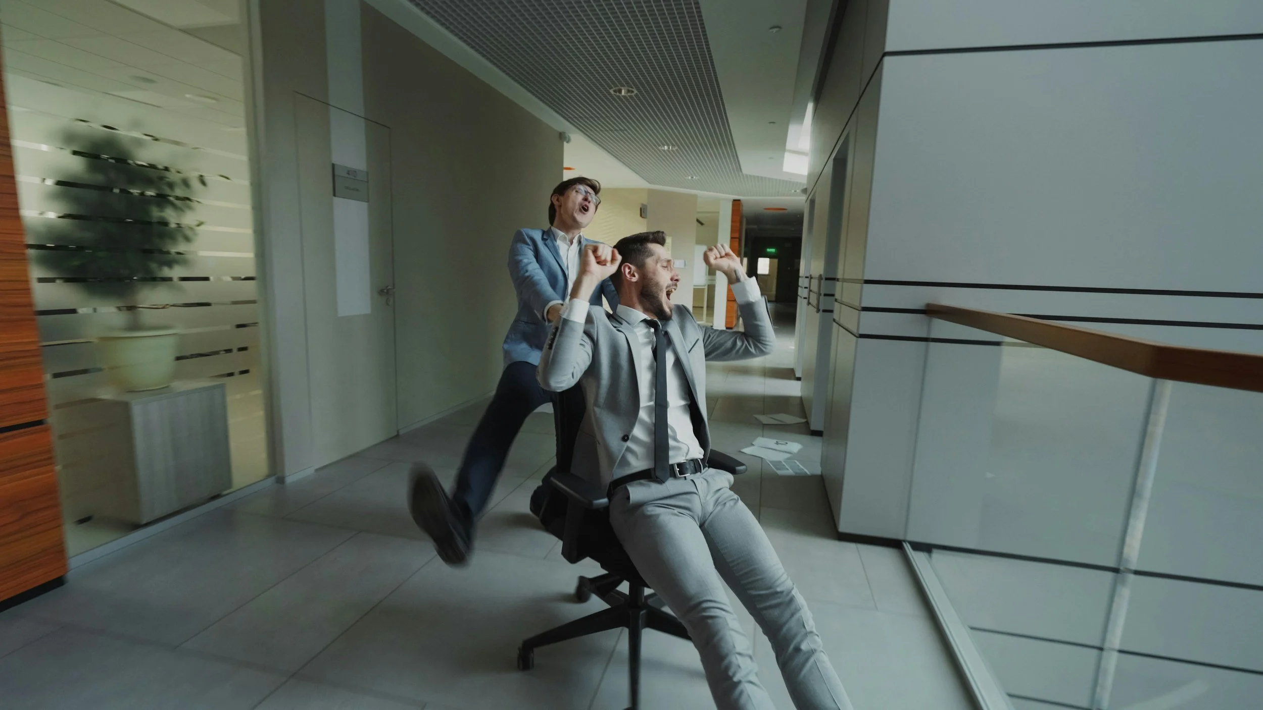Office workers racing chairs down a corridor, reflecting workplace chaos