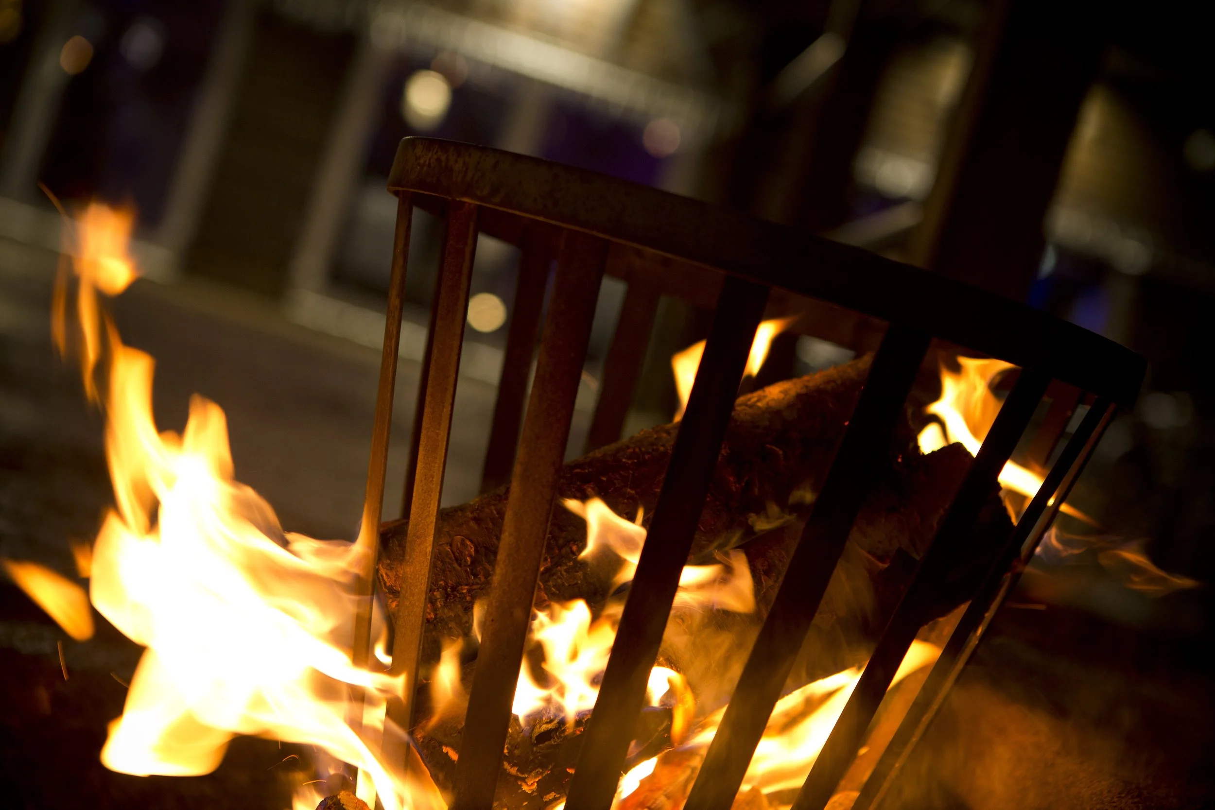 A fire burning in a metal fire basket with logs inside, with visible flames and embers.