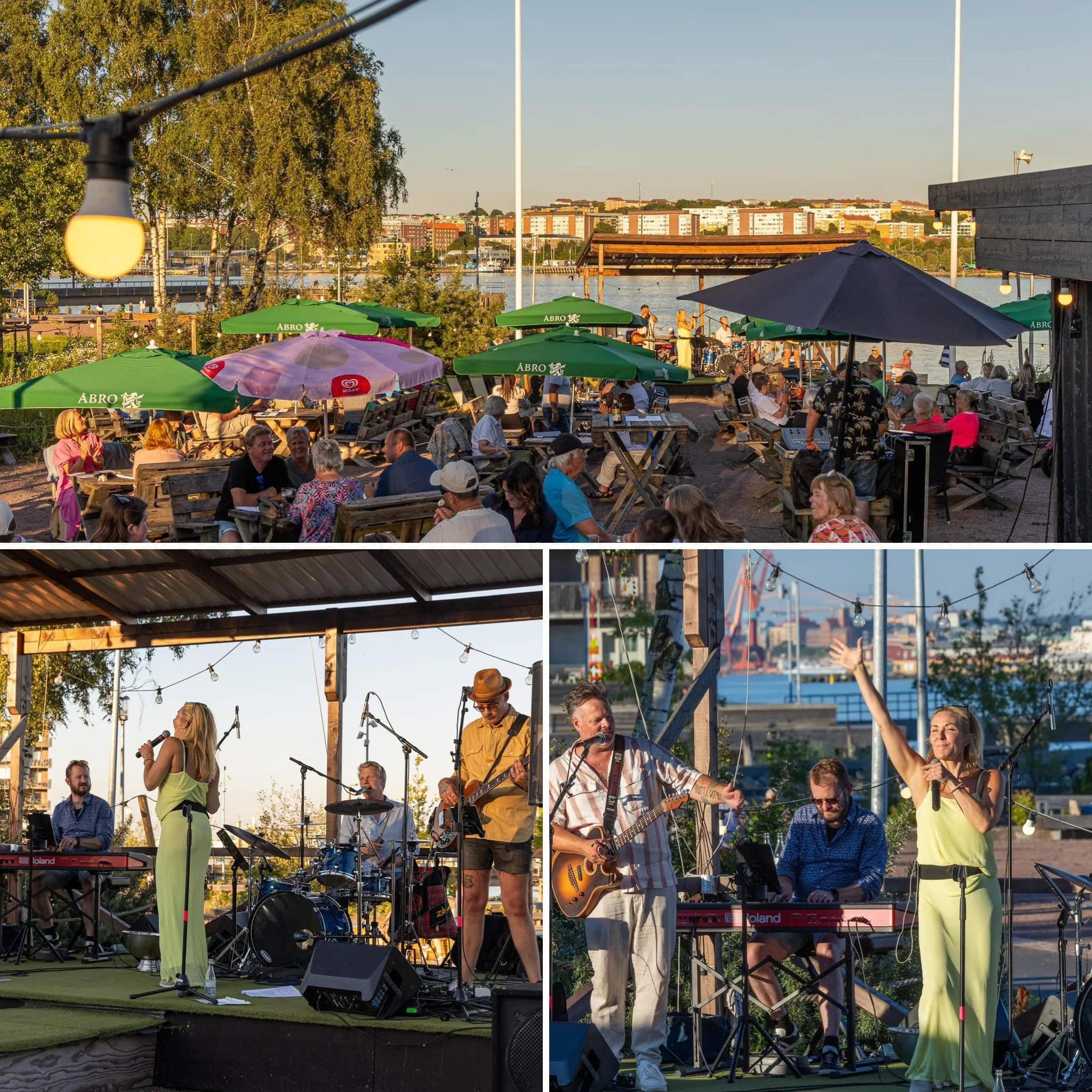 An outdoor live music performance at a waterfront venue during sunset. The scene shows a band with a woman singer, guitarist, keyboardist, and drummer performing on stage. Audience members sit and stand, enjoying the music under umbrellas and string 