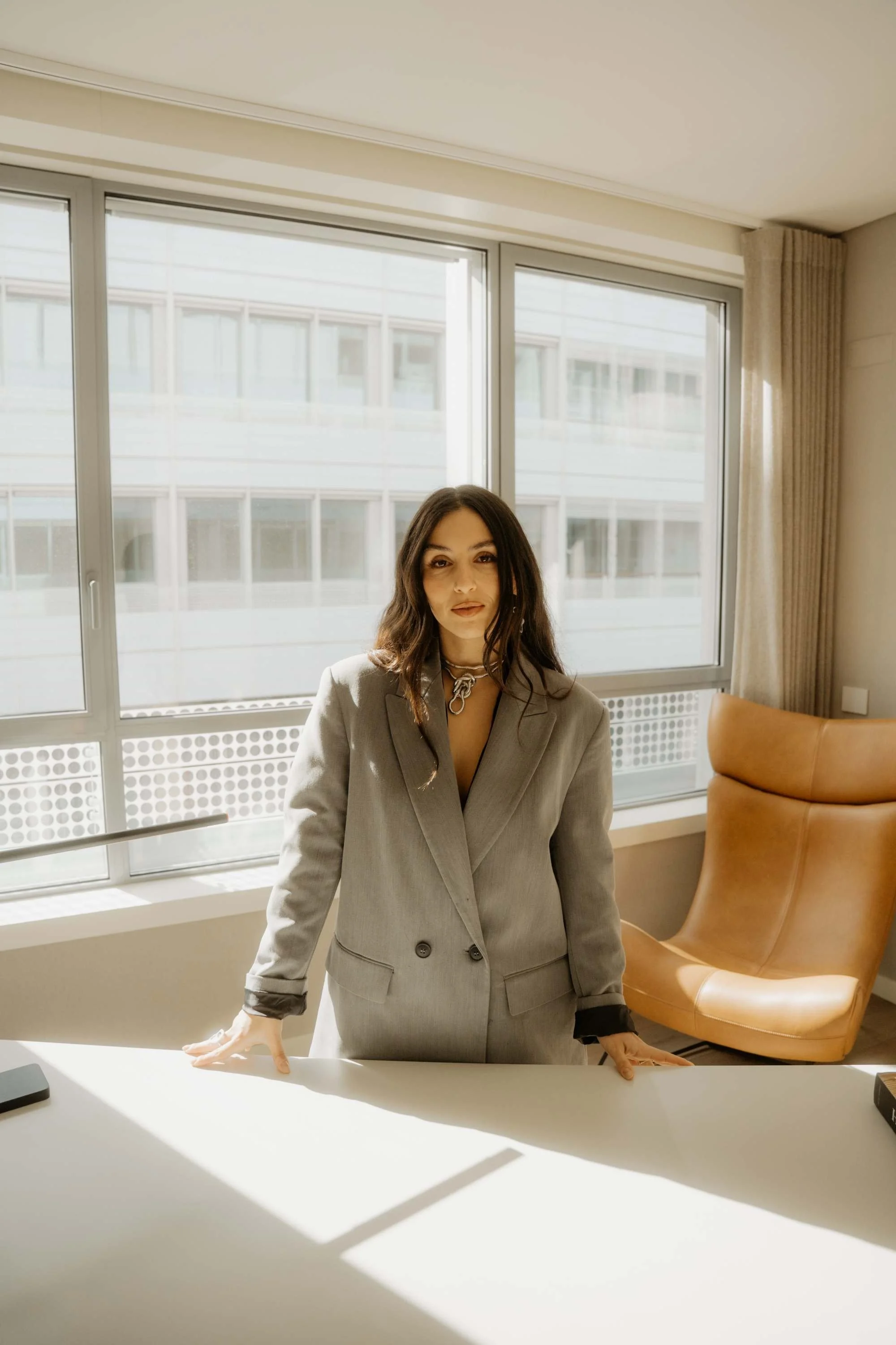 Fabiana Trudu, Head of Architecture & Advisory at Hillforte. A woman stands behind a white table in an office, wearing a gray suit, with sunlight coming through large windows behind her.