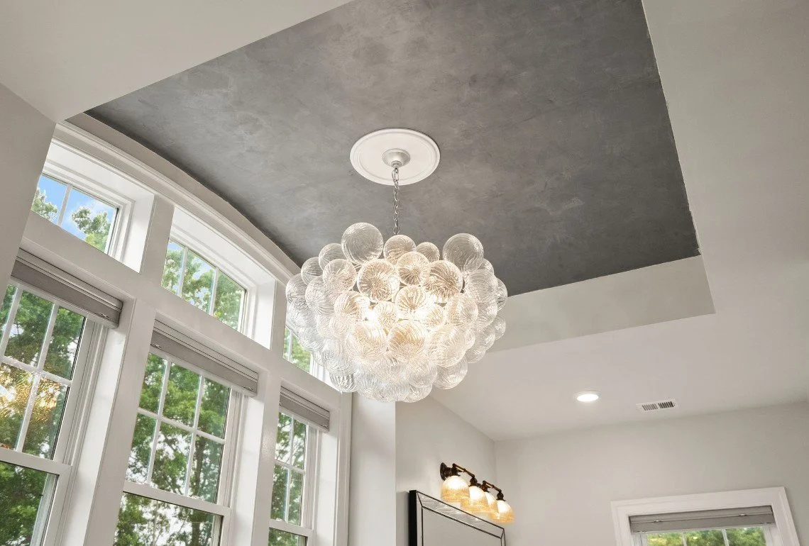 Modern interior ceiling with a cluster chandelier made of glass globes, large windows, and white walls.