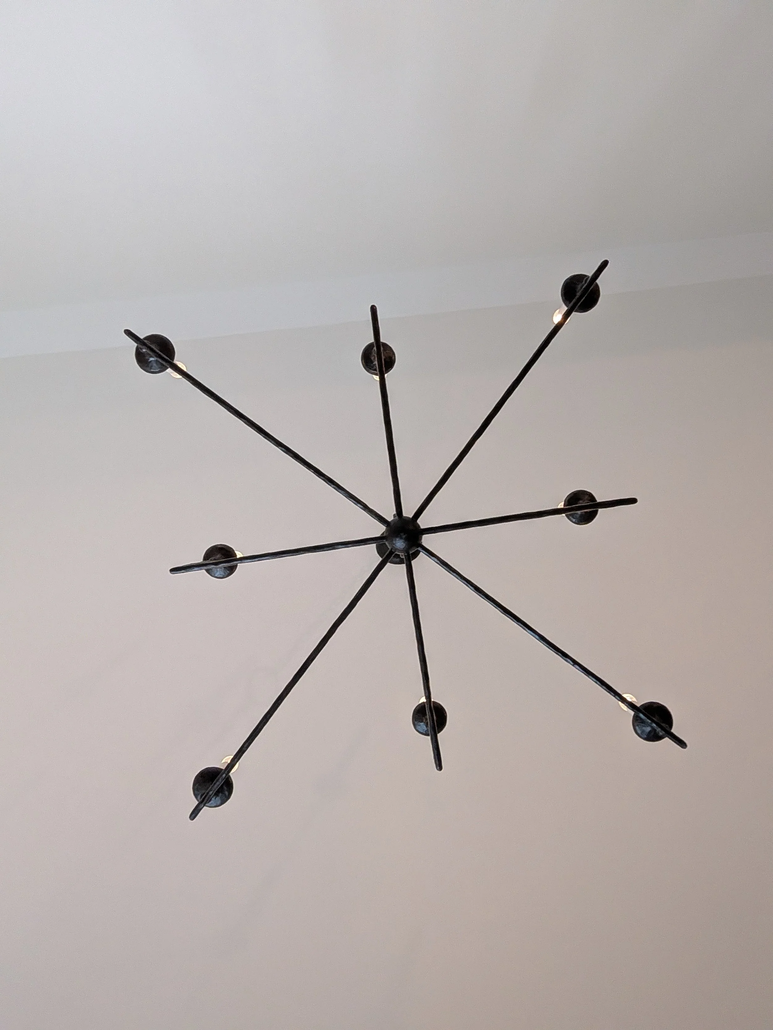 A modern black chandelier with multiple arms extending from a central point, each with a small spherical light bulb at the end.