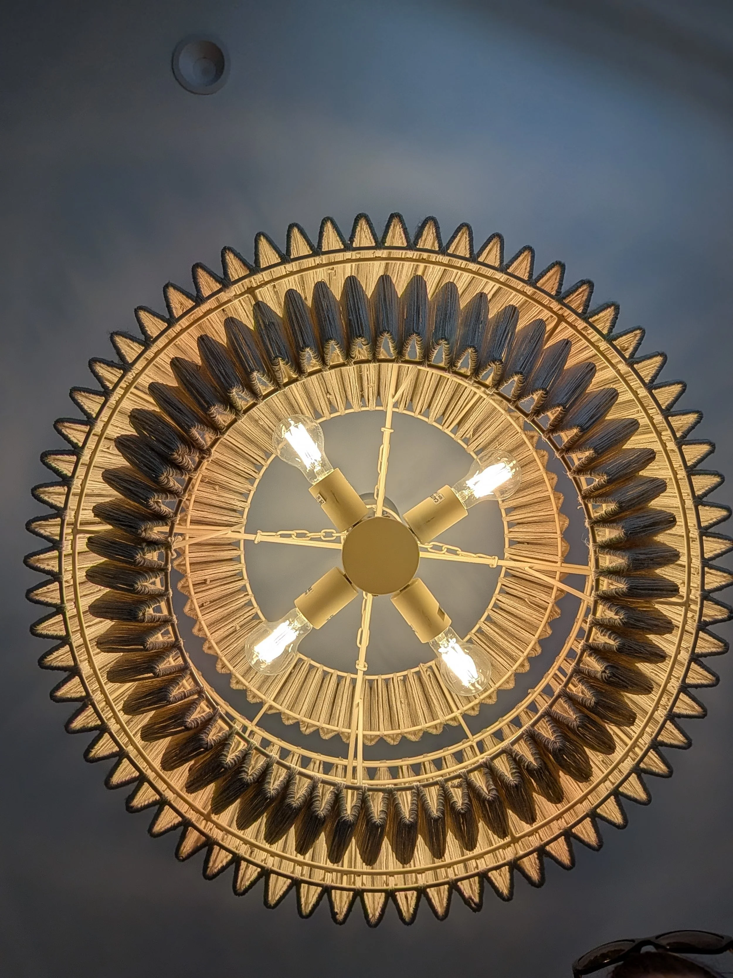 Decorative circular chandelier with wood and metal elements, four exposed light bulbs, hanging from a chain, mounted on a gray ceiling.
