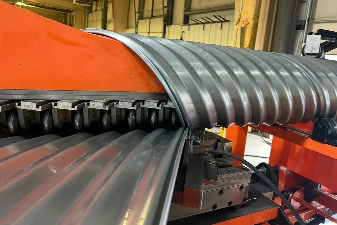 A metal coil rolling machine shaping a large sheet of metal into a curved form.