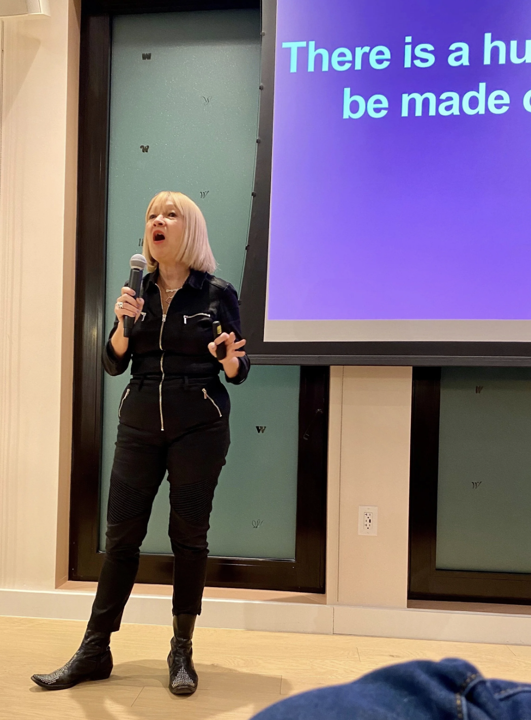 Cindy Gallop, a petite but powerful blonde woman in a black jumpsuit, holds a microphone and speaks
