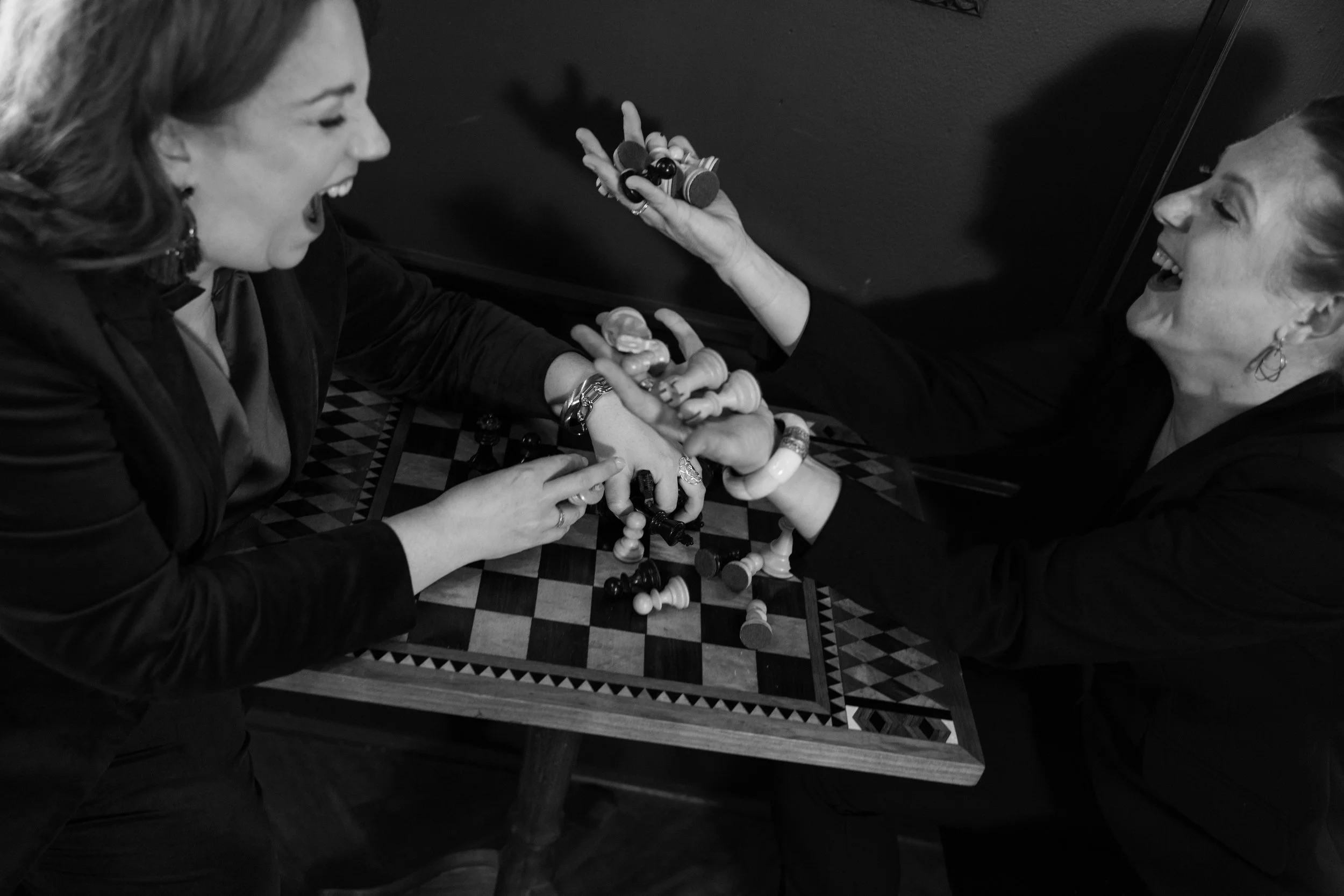 Two women playing a lively game of chess at a small table, laughing and enjoying each other's company.