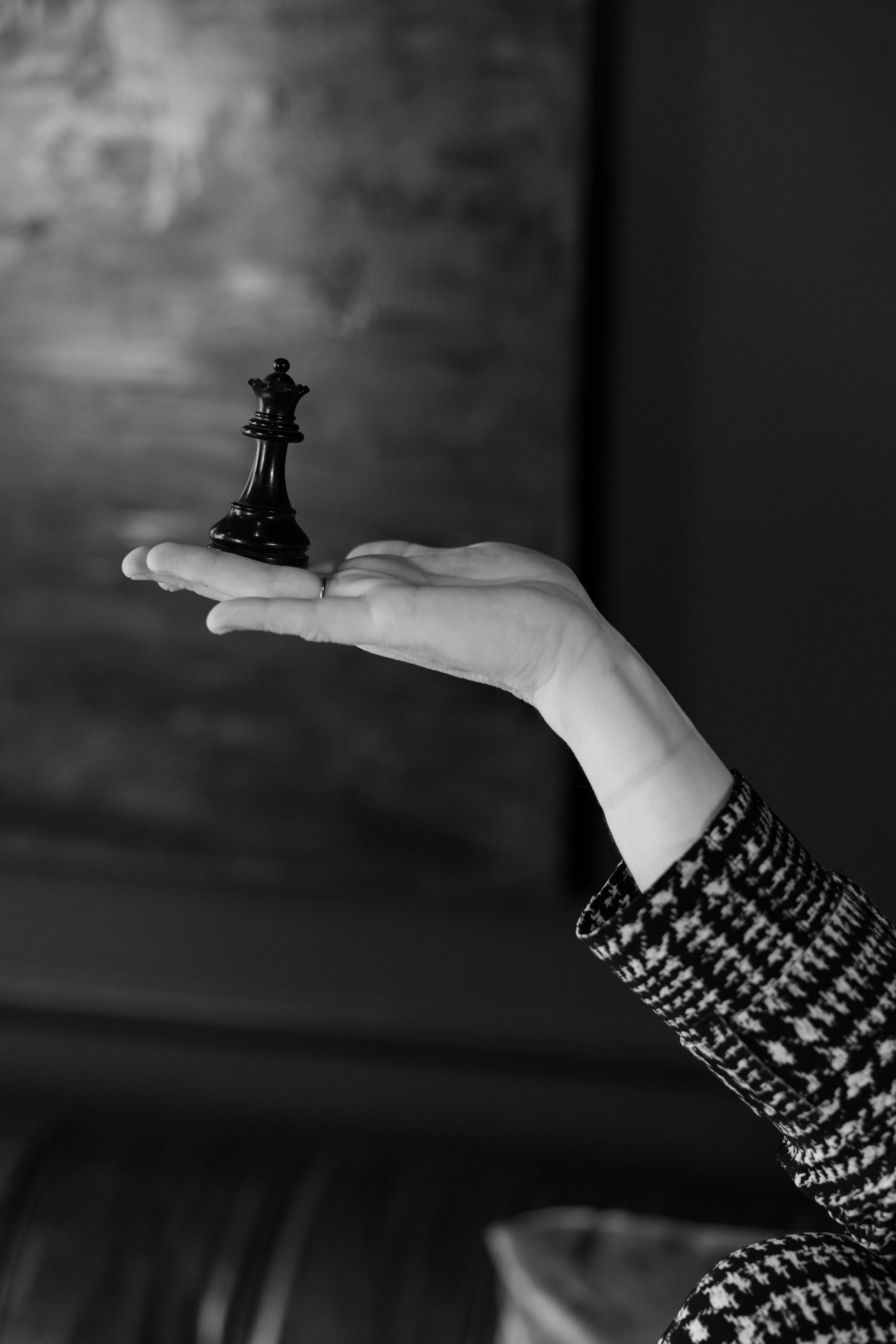 A hand holding a small black chess king piece, with a blurred background.