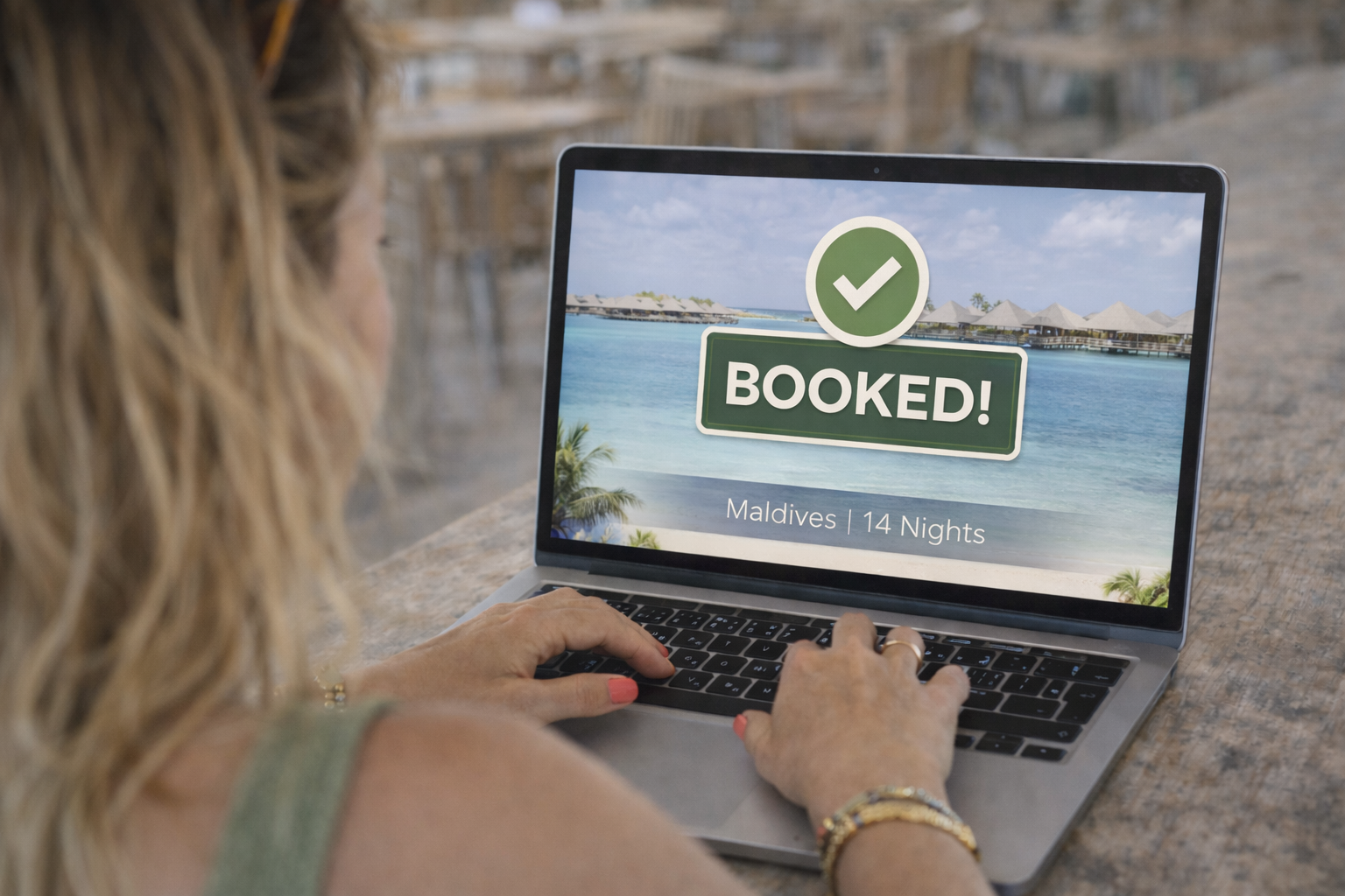 A woman is looking at a laptop screen displaying a confirmation message that reads 'BOOKED!' with a green checkmark, indicating a reservation for a 14-night stay in the Maldives.
