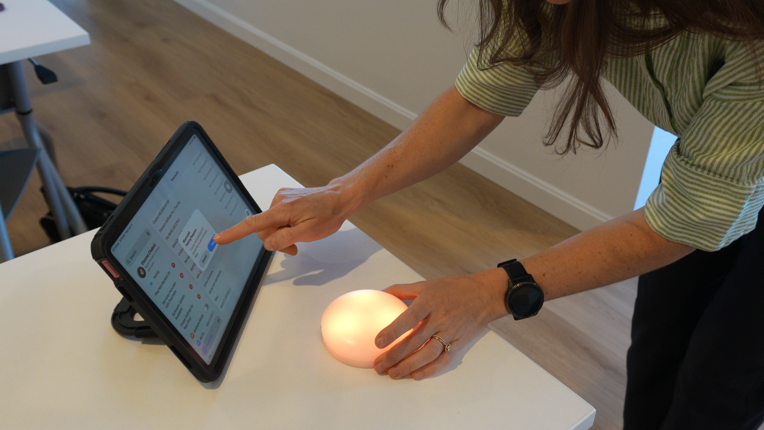 Person using a smartphone at a white table, with a candle nearby. The person is wearing a striped shirt and a watch, and has long brown hair.
