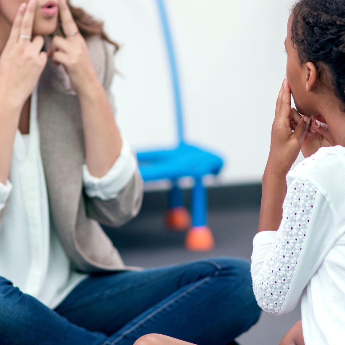 Two women in a therapy session sitting on the floor, making hand gestures to communicate.
