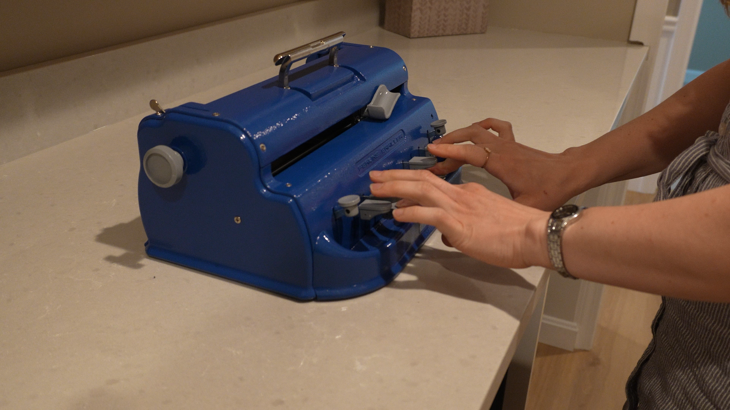 People using a blue vintage typewriter on a beige countertop.