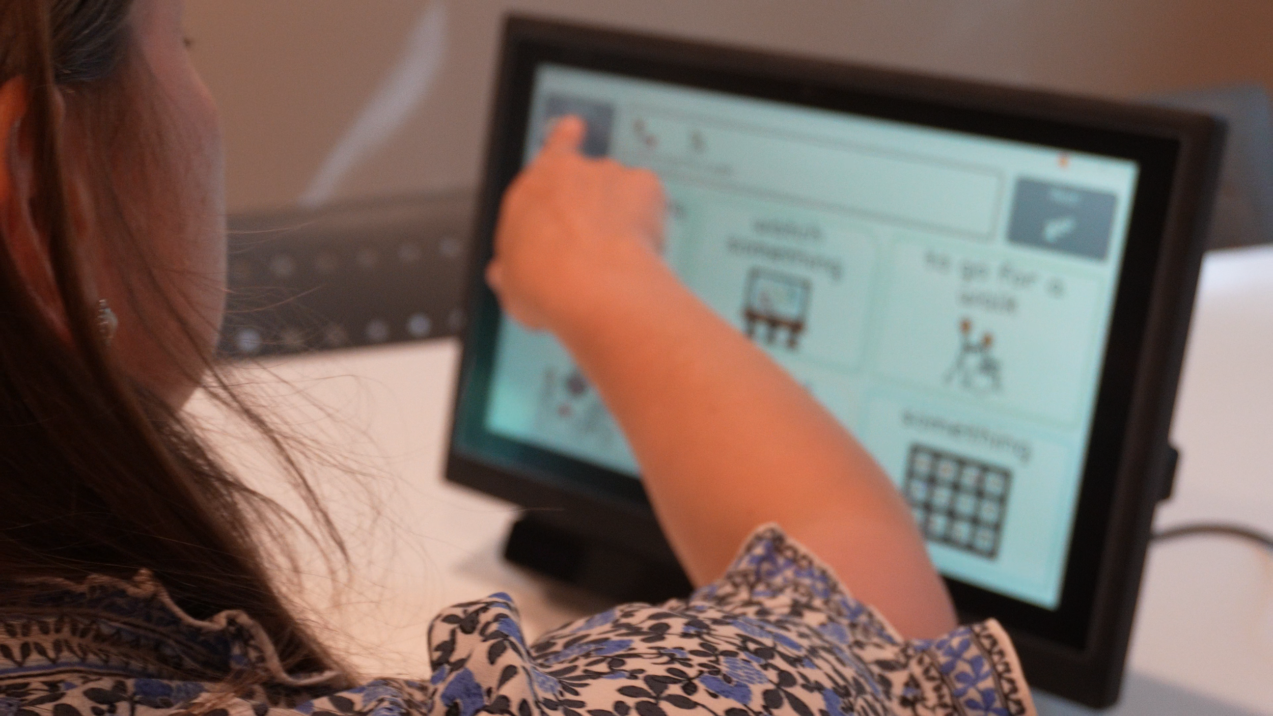A woman with brown hair and a floral-patterned shirt using a touchscreen computer, with her hand touching the screen.