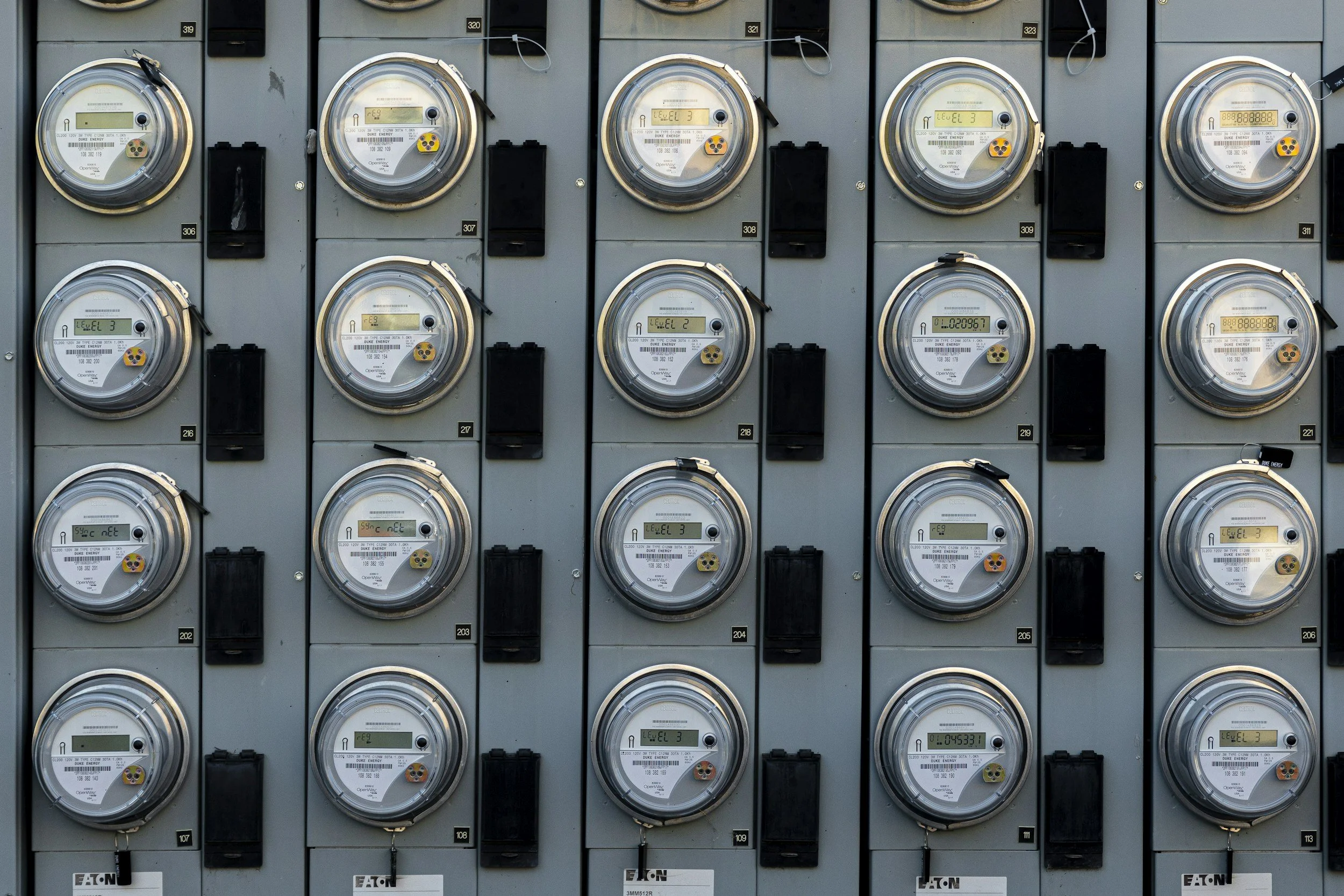 Multiple electric utility meters mounted on a gray panel, each with digital or analog displays used to measure electricity consumption.